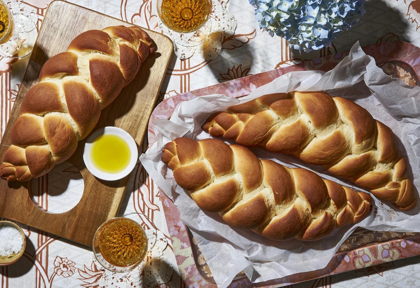 Three loaves of water challah with dishes of maple syrup and coarse salt, glasses of white wine, and fresh flowers.
