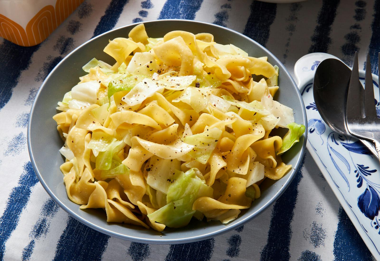 Noodles and cabbage with cracked pepper in blue bowl, atop blue and white tablecloth.