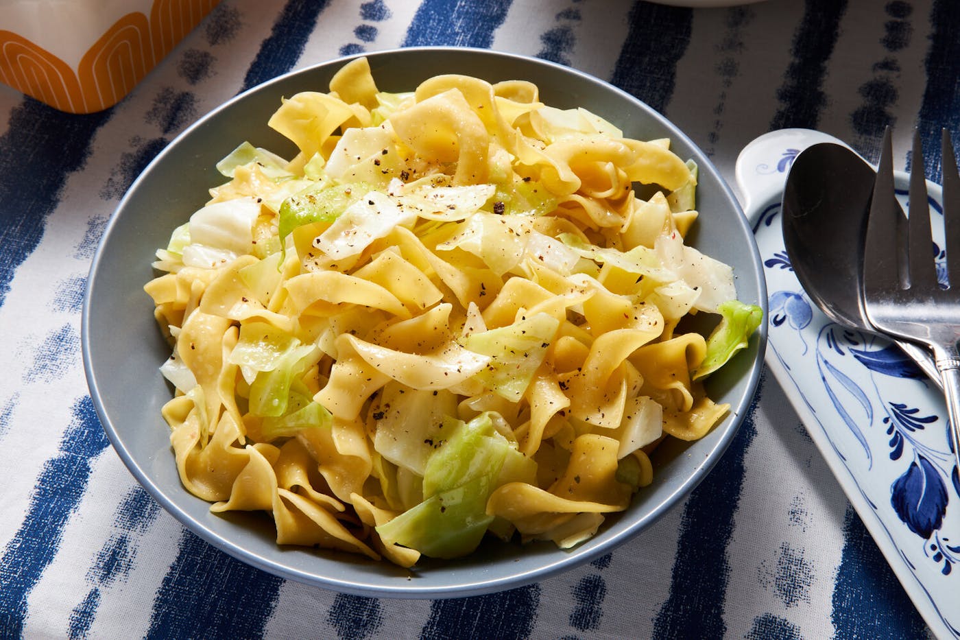 Noodles and cabbage with cracked pepper in blue bowl, atop blue and white tablecloth.