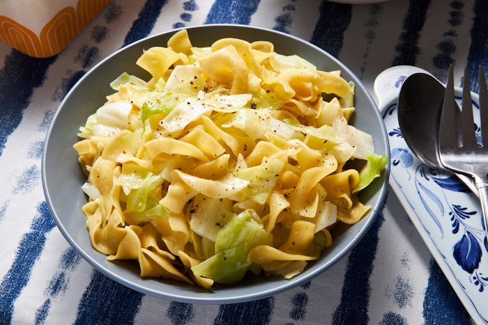 Noodles and cabbage with cracked pepper in blue bowl, atop blue and white tablecloth.