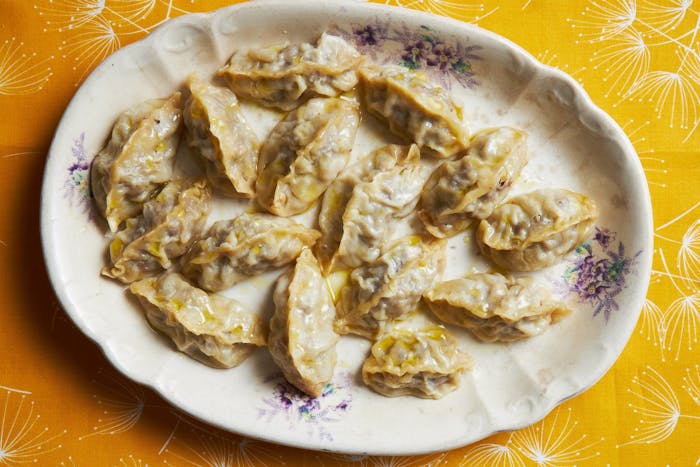 Manti drizzled with olive oil on white plate atop bright orange tablecloth.
