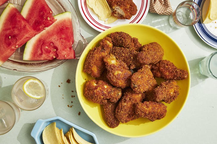 Fried chicken wings in yellow bowl next to sliced watermelon and potato chips.