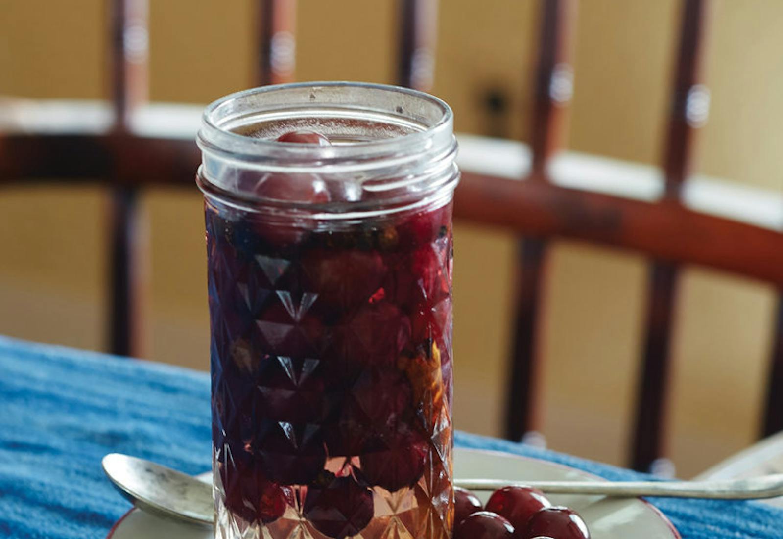 Pickled grapes with cardamom in pickling jar on white dish atop blue tablecloth.