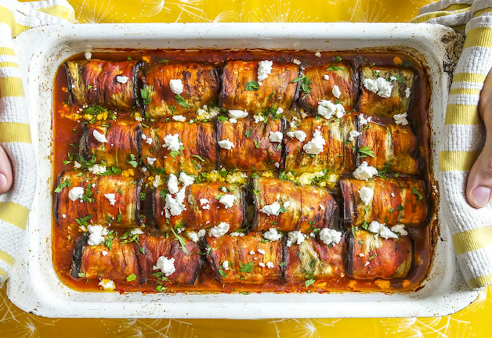 Chef holding pan of eggplant dolmas garnished with feta and chopped parsley.