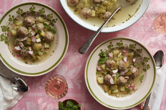 Bowls of hamod with fresh radish and mint, glasses of white wine, atop pink tablecloth.