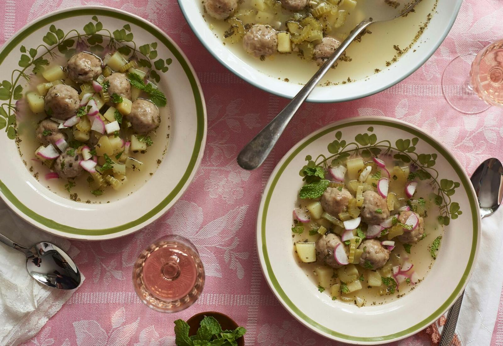 Bowls of hamod with fresh radish and mint, glasses of white wine, atop pink tablecloth.