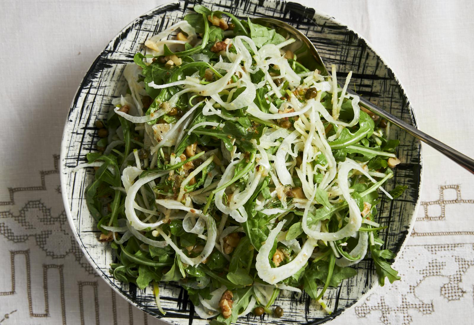 Arugula salad with shaved fennel in black and white striped bowl.