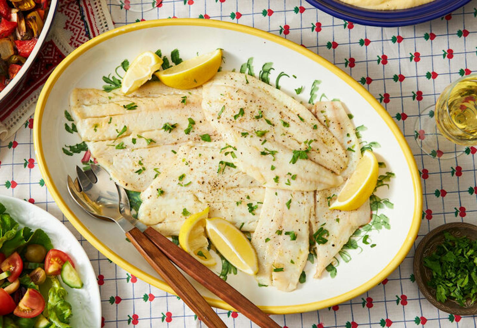 Fried Sole with lemon wedges and parsley, white wine and green salad atop fruit-patterned tablecloth.