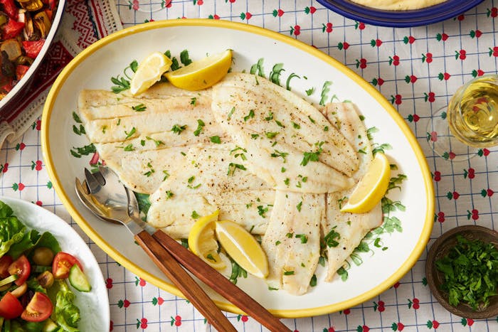 Fried Sole with lemon wedges and parsley, white wine and green salad atop fruit-patterned tablecloth.