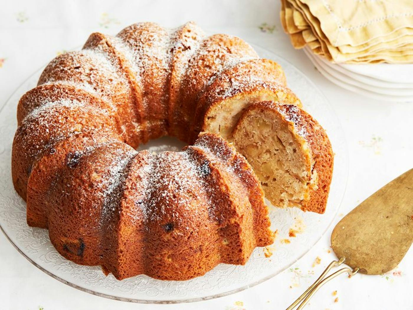 Apple cake with powdered sugar, gold pie server and yellow napkins. 