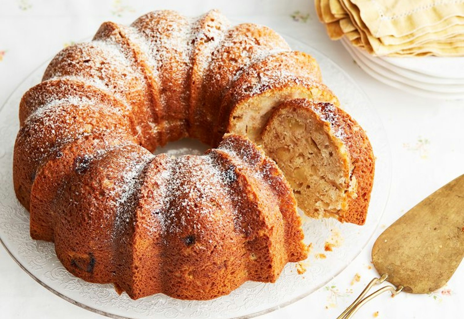 Apple cake with powdered sugar, gold pie server and yellow napkins. 