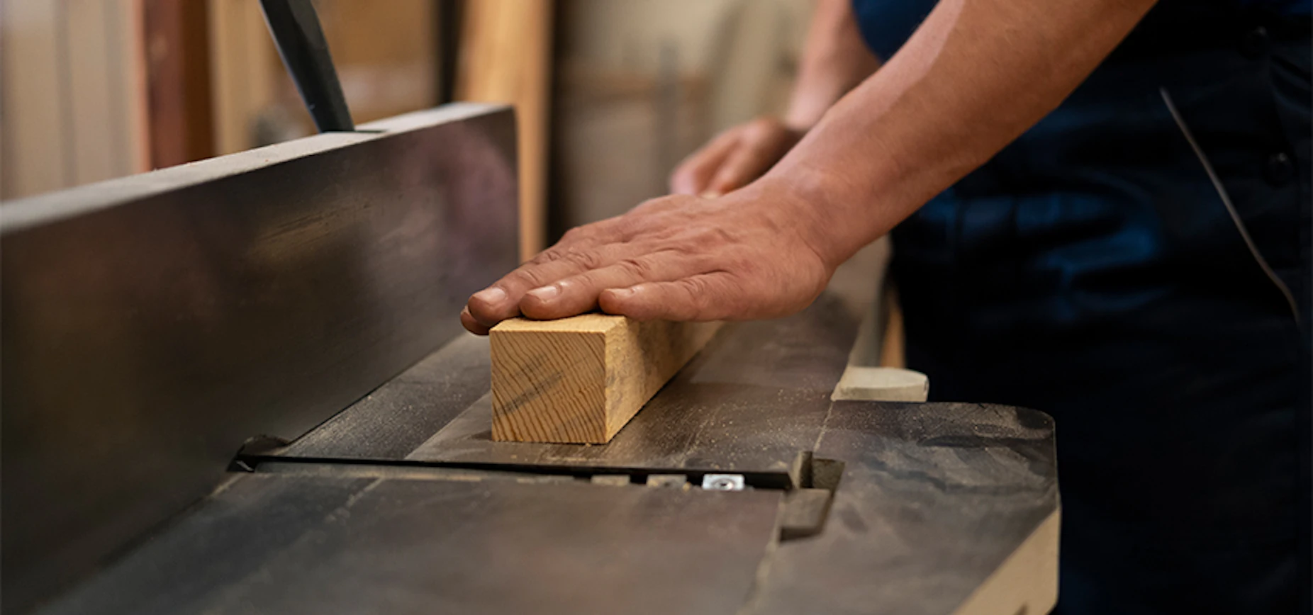 worker holding a small piece of lumber on a saw