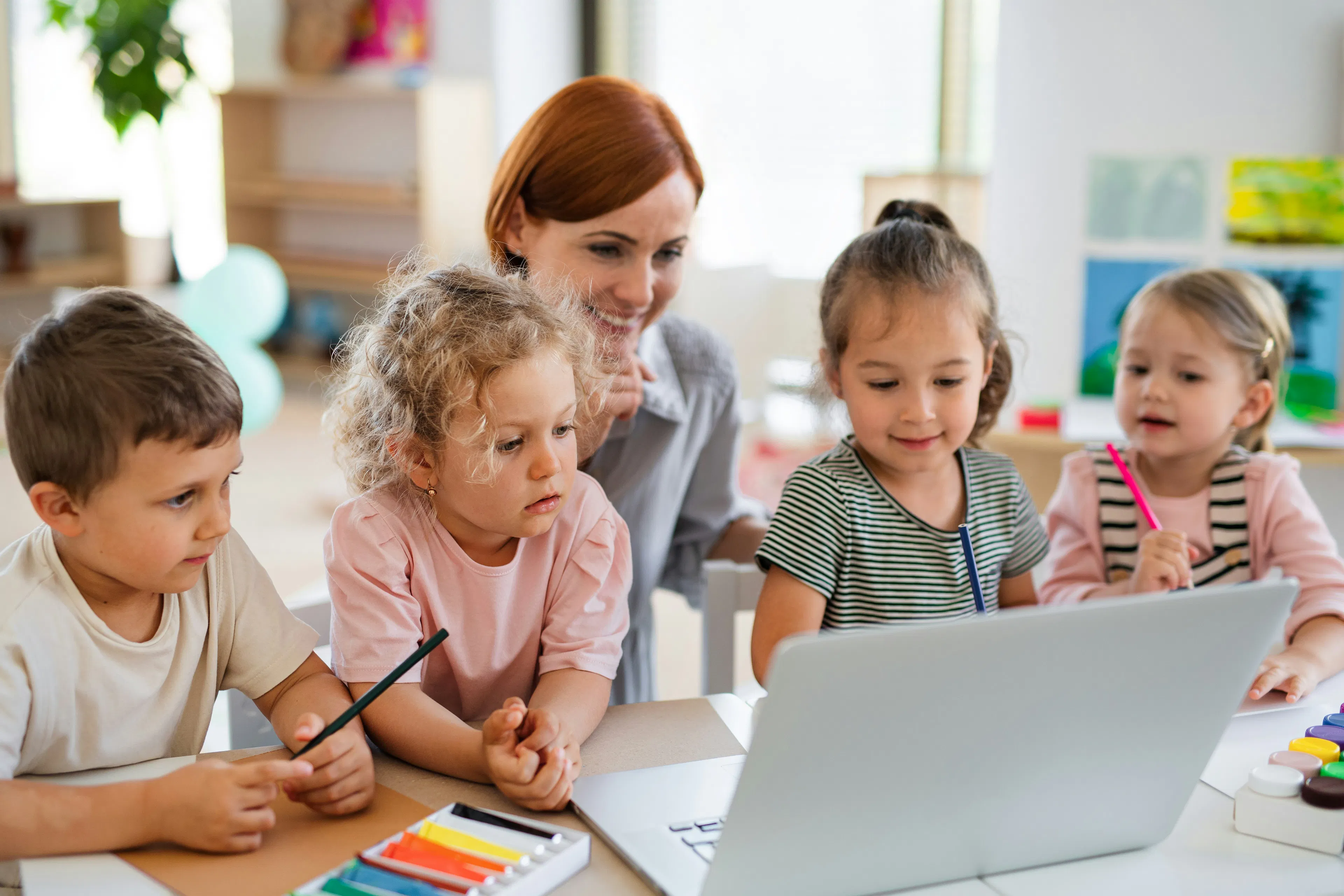 smiling woman with red hair sitting with four children at a laptop