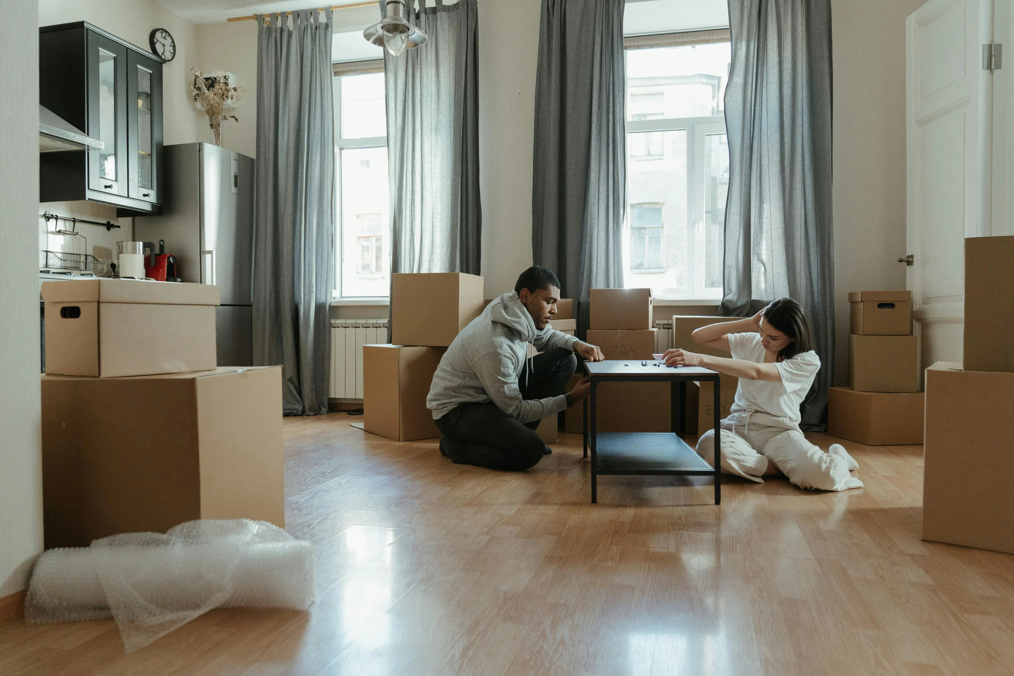 A young couple sitting in a living room surrounded by moving boxes