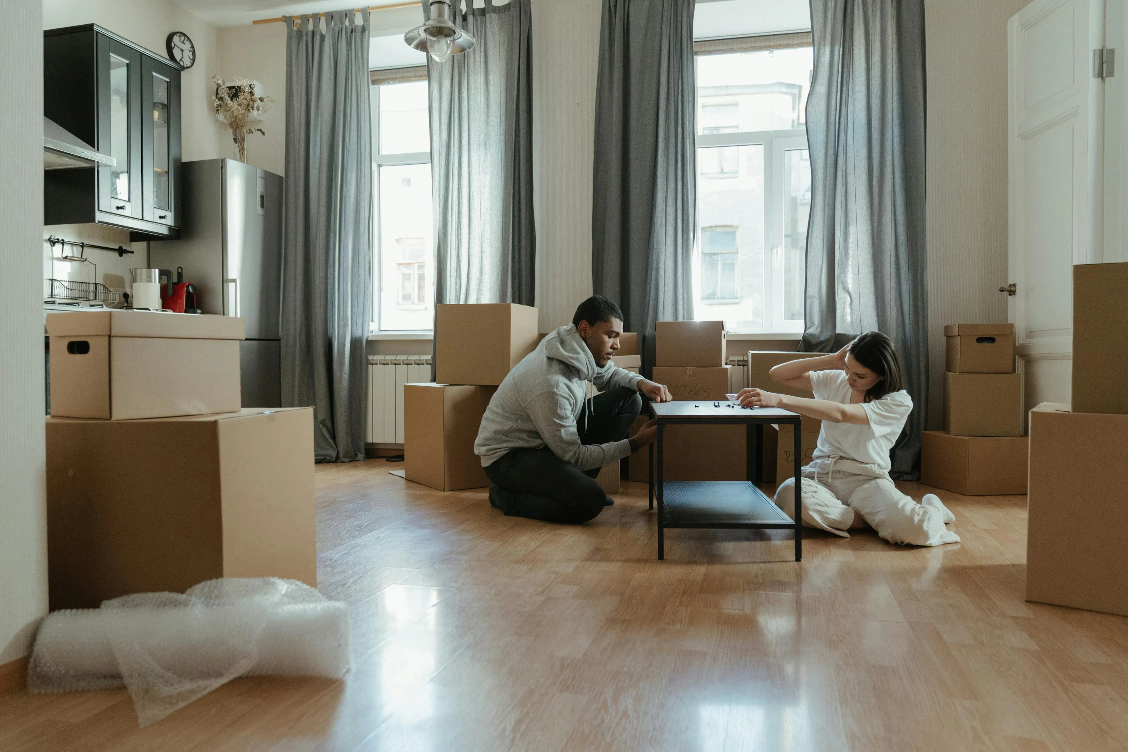 A young couple sitting in a living room surrounded by moving boxes