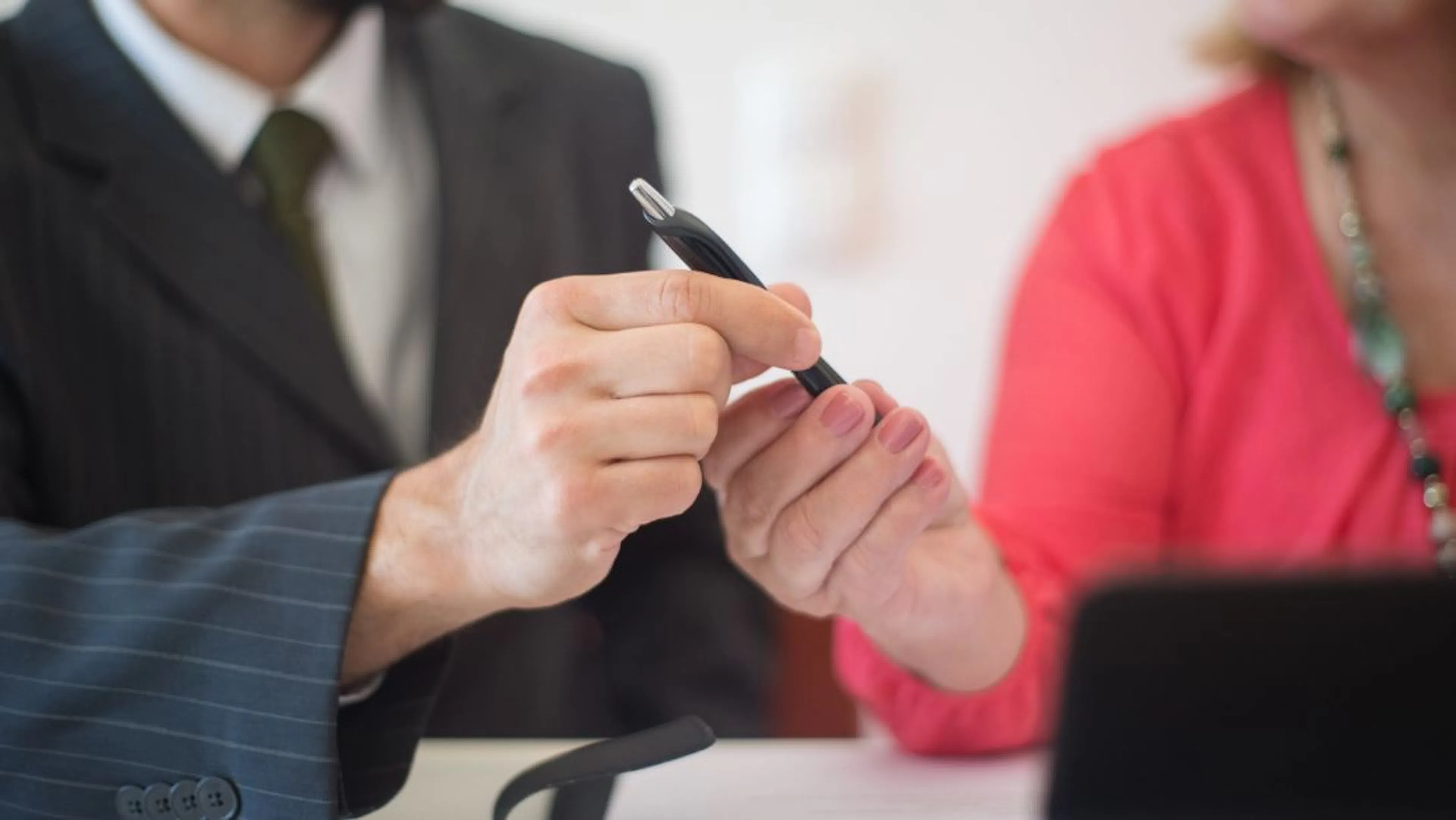 Two businesspeople exchange a pen to sign a contract