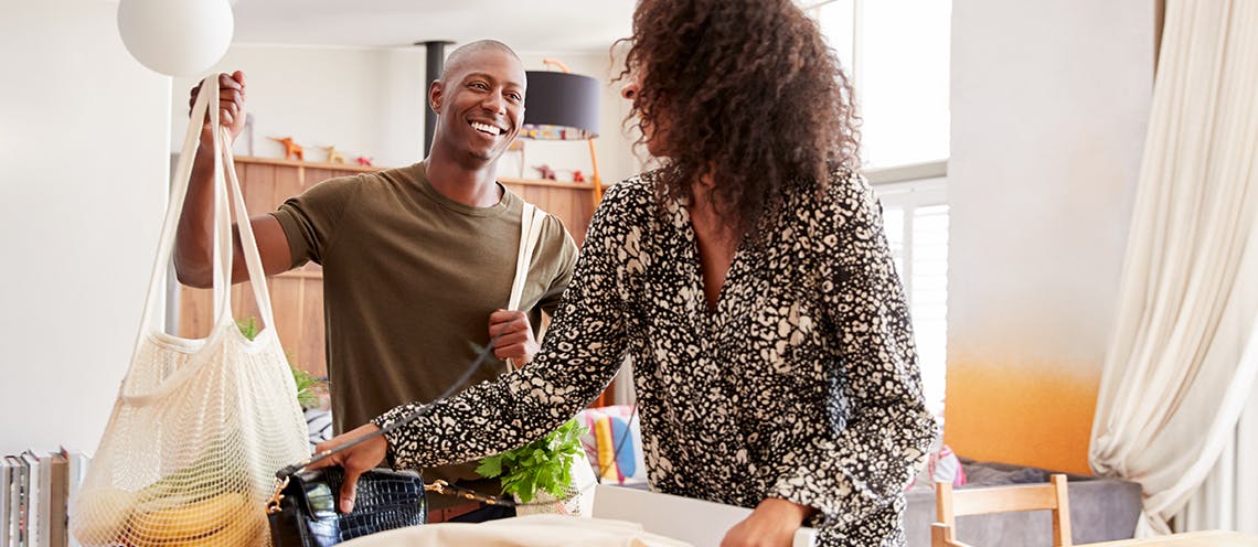 An image of a man and woman smiling and holding a bag of groceries.