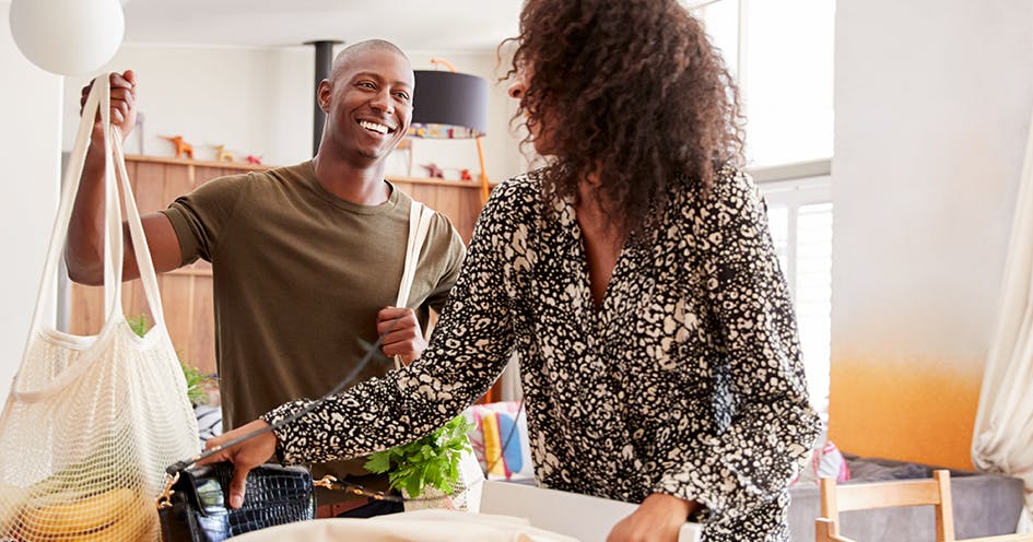 An image of a man and woman smiling and holding a bag of groceries.