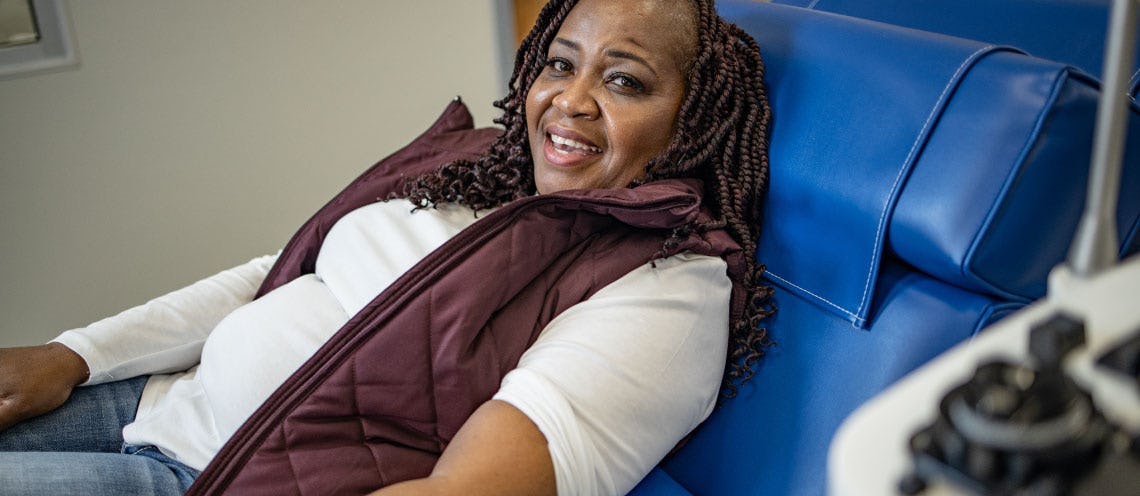 Image of a smiling woman laying on a blue donation bed at a blood donation center.