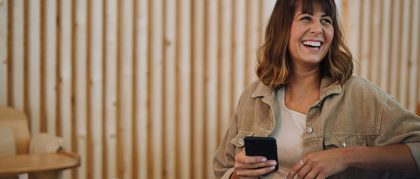 Photo of woman laughing while reading her phone.
