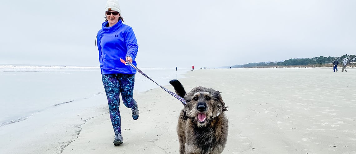 Image of woman running on beach with a dog.