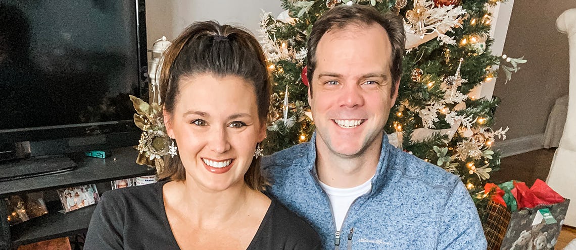Image of man and woman smiling in front of a Christmas tree