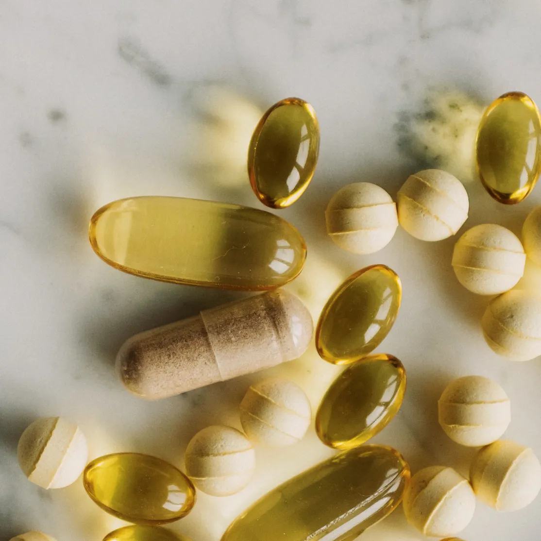 A close-up image of an array of yellow, gold, and tan supplements on a marble counter.