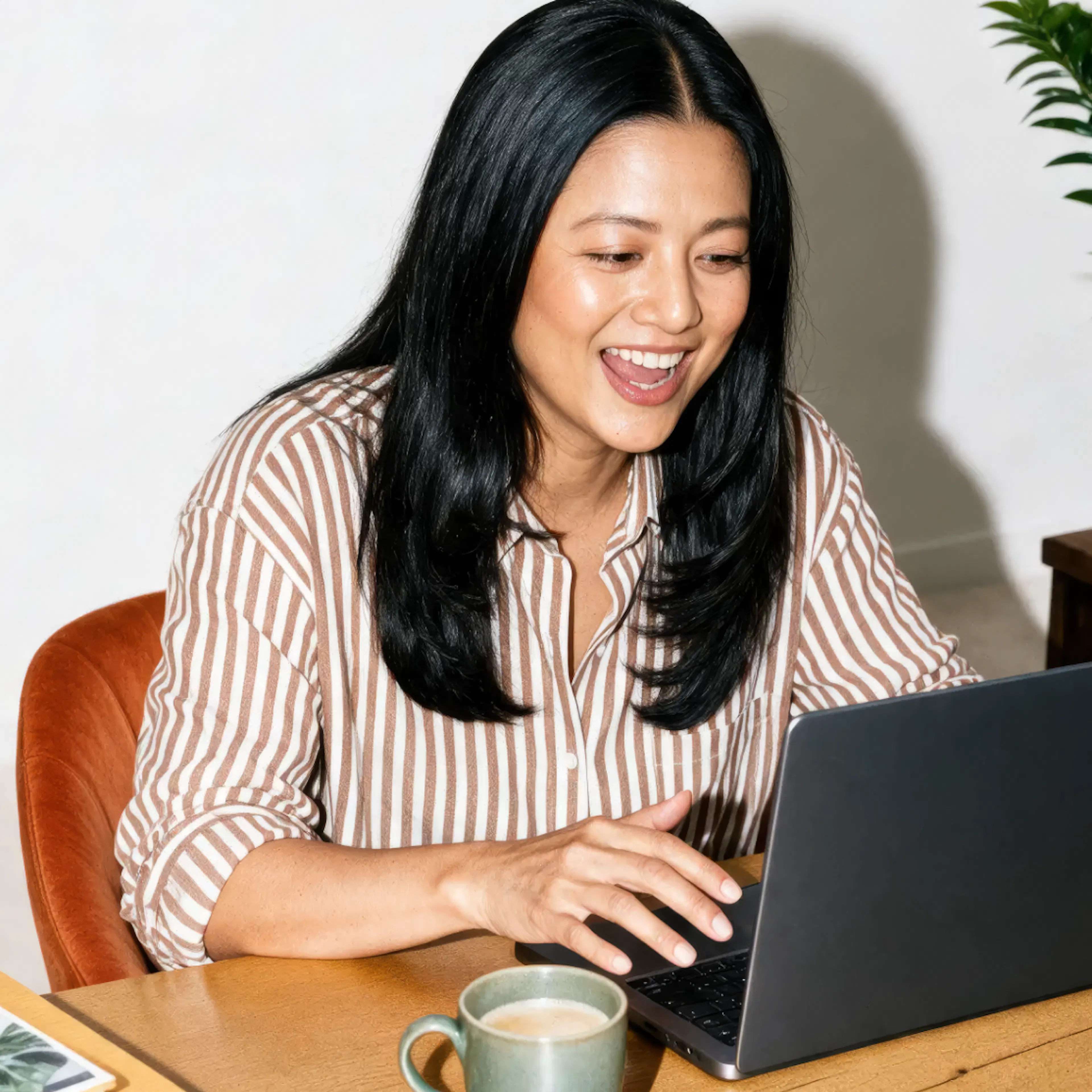 A woman in midlife smiling while typing on her laptop.
