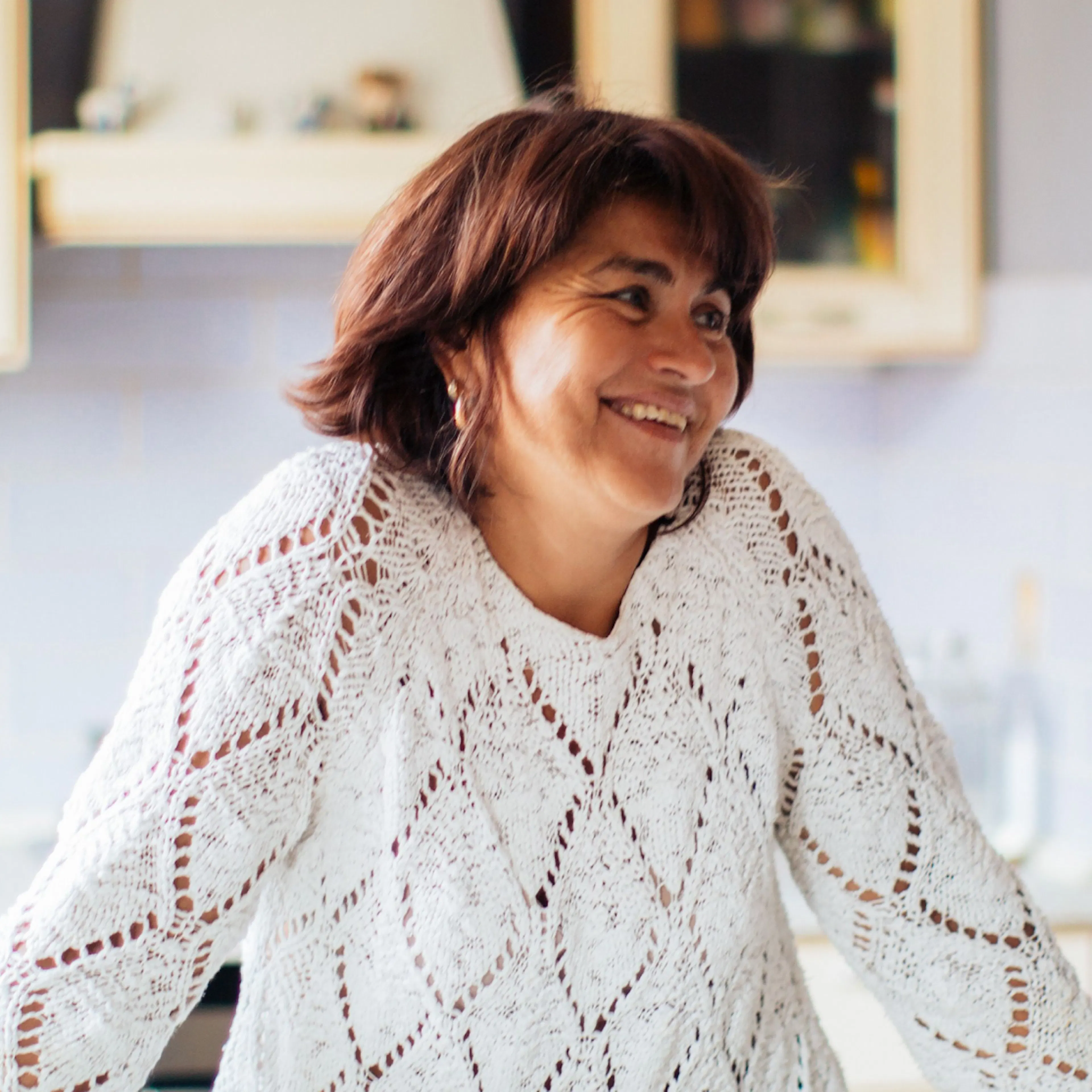 A woman in midlife, smiling and looking to the side, with a white sweater on.
