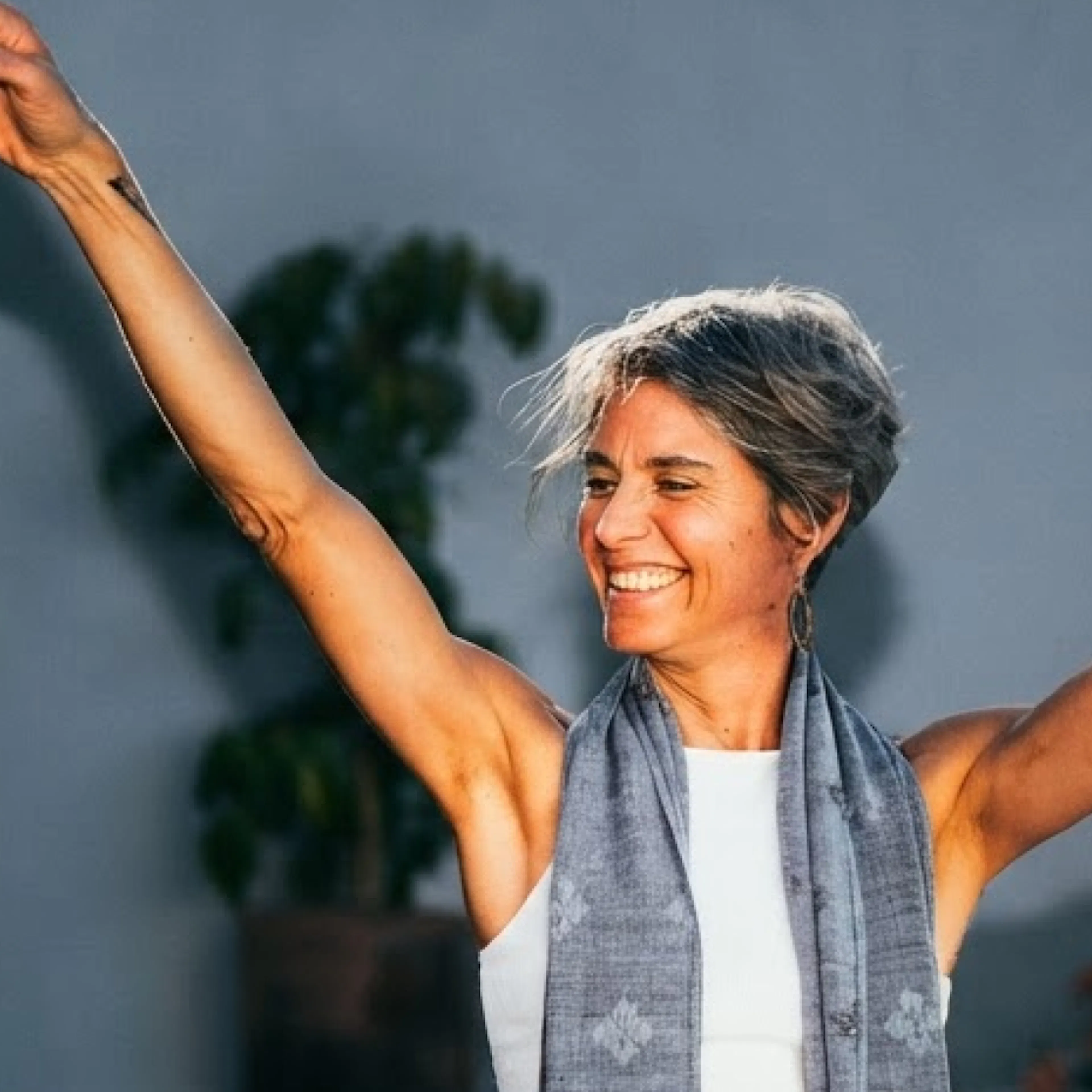  A woman in midlife standing outside, smiling and stretching her hands in the air, happy she's experiencing signs metformin is working.