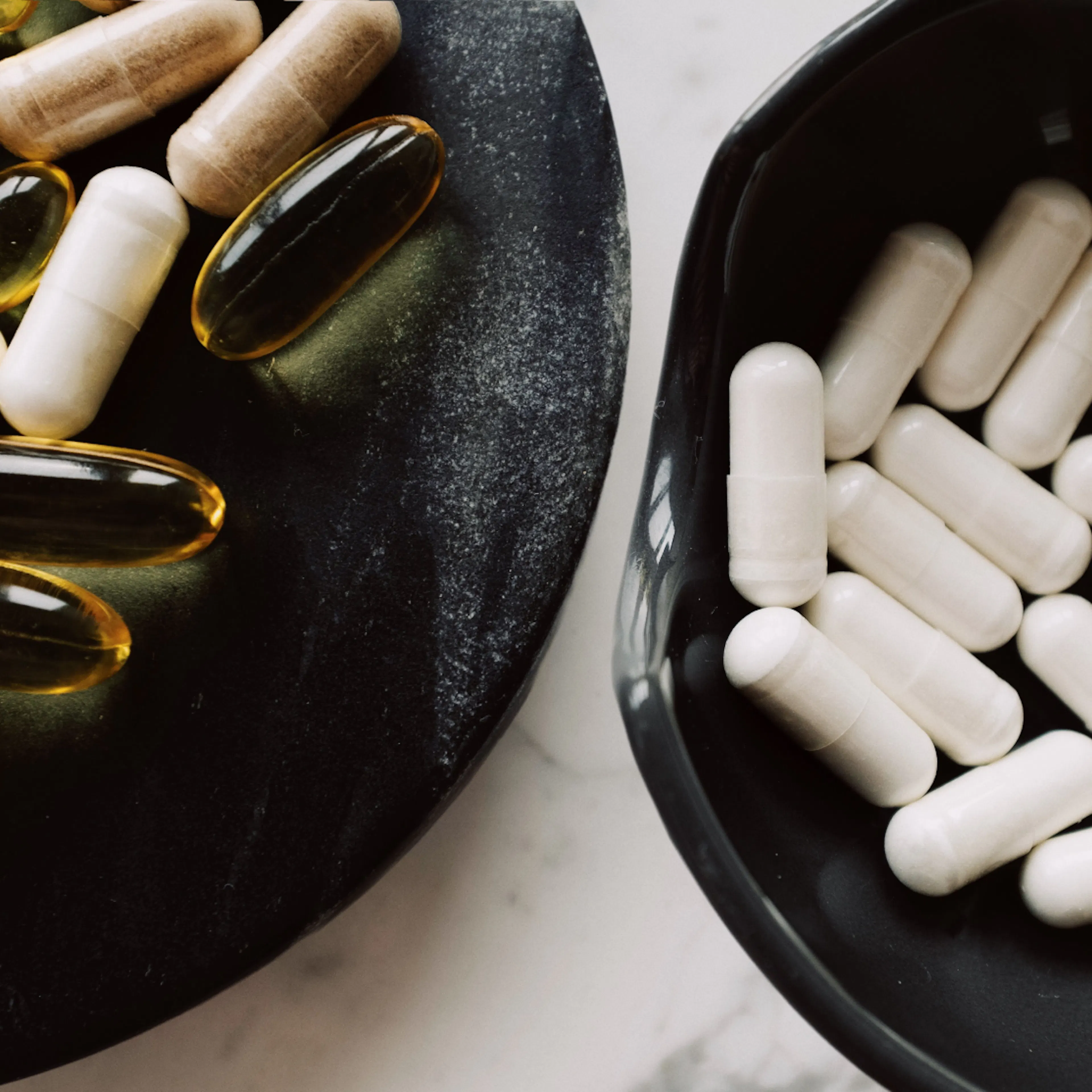 Two bowls of supplements sitting side by side on a marble surface.