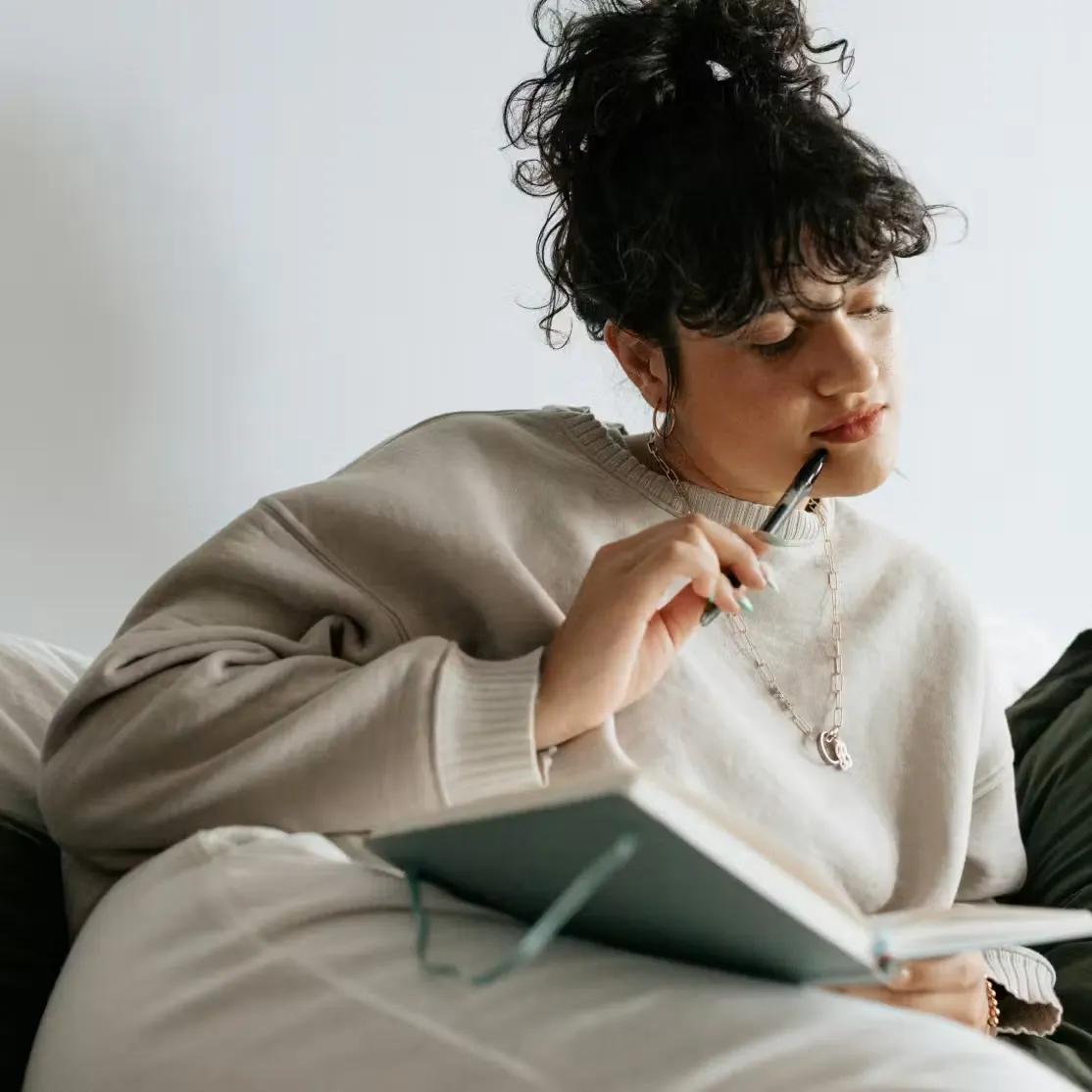 Woman with curly hair holding pen thoughtfully over open notebook