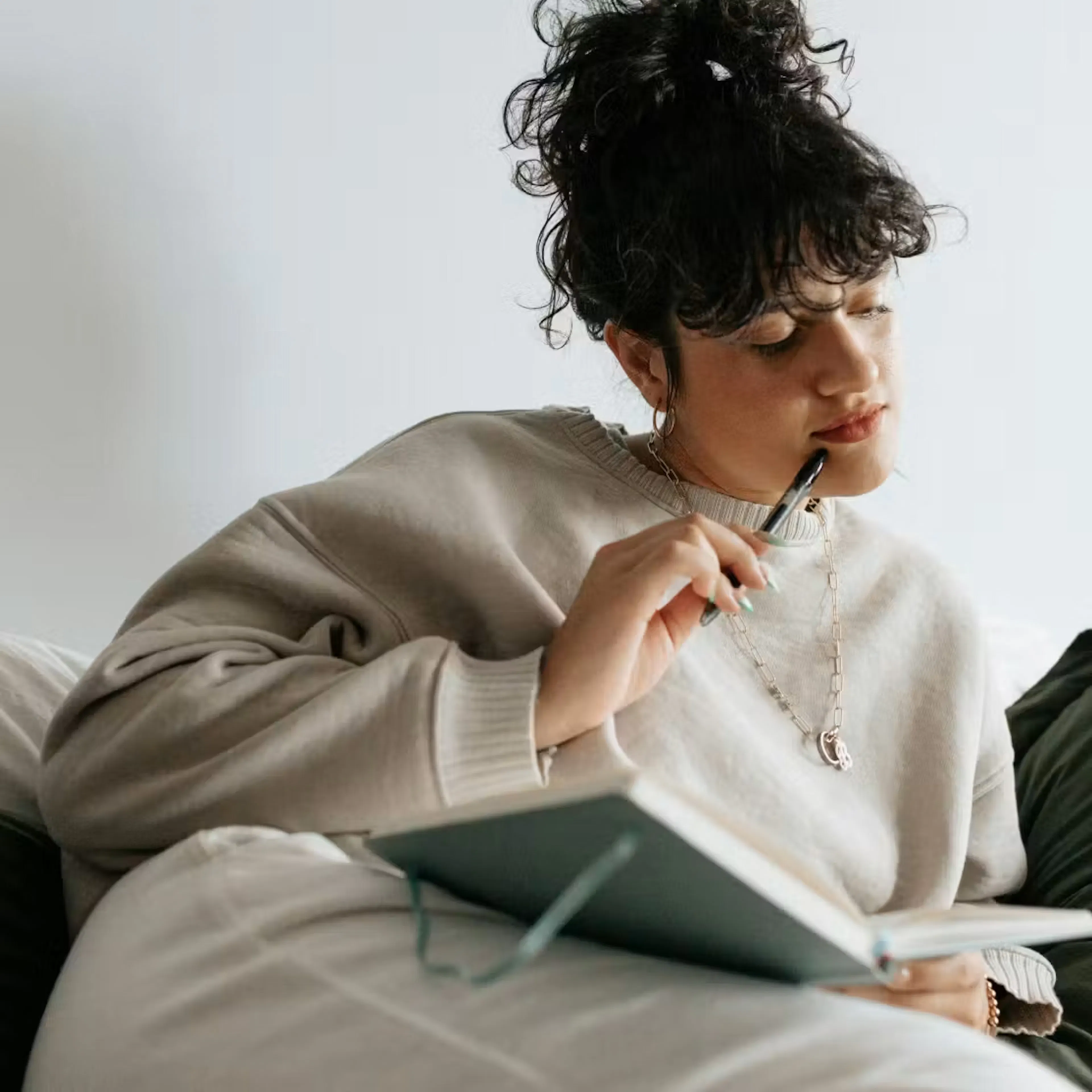 Woman with curly hair holding pen thoughtfully over open notebook
