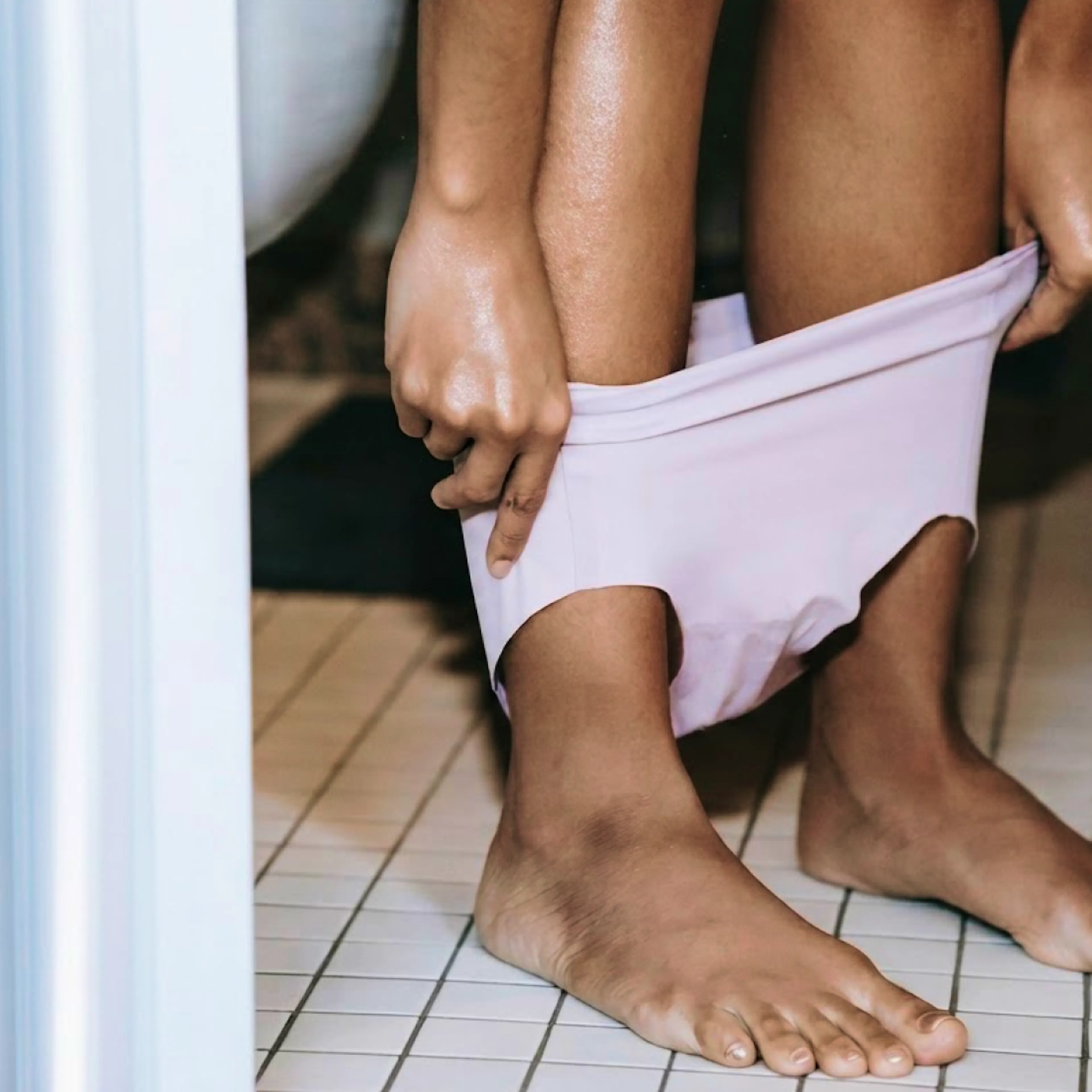 A close-up photo of a woman's underwear around her ankles as she stands in the background.