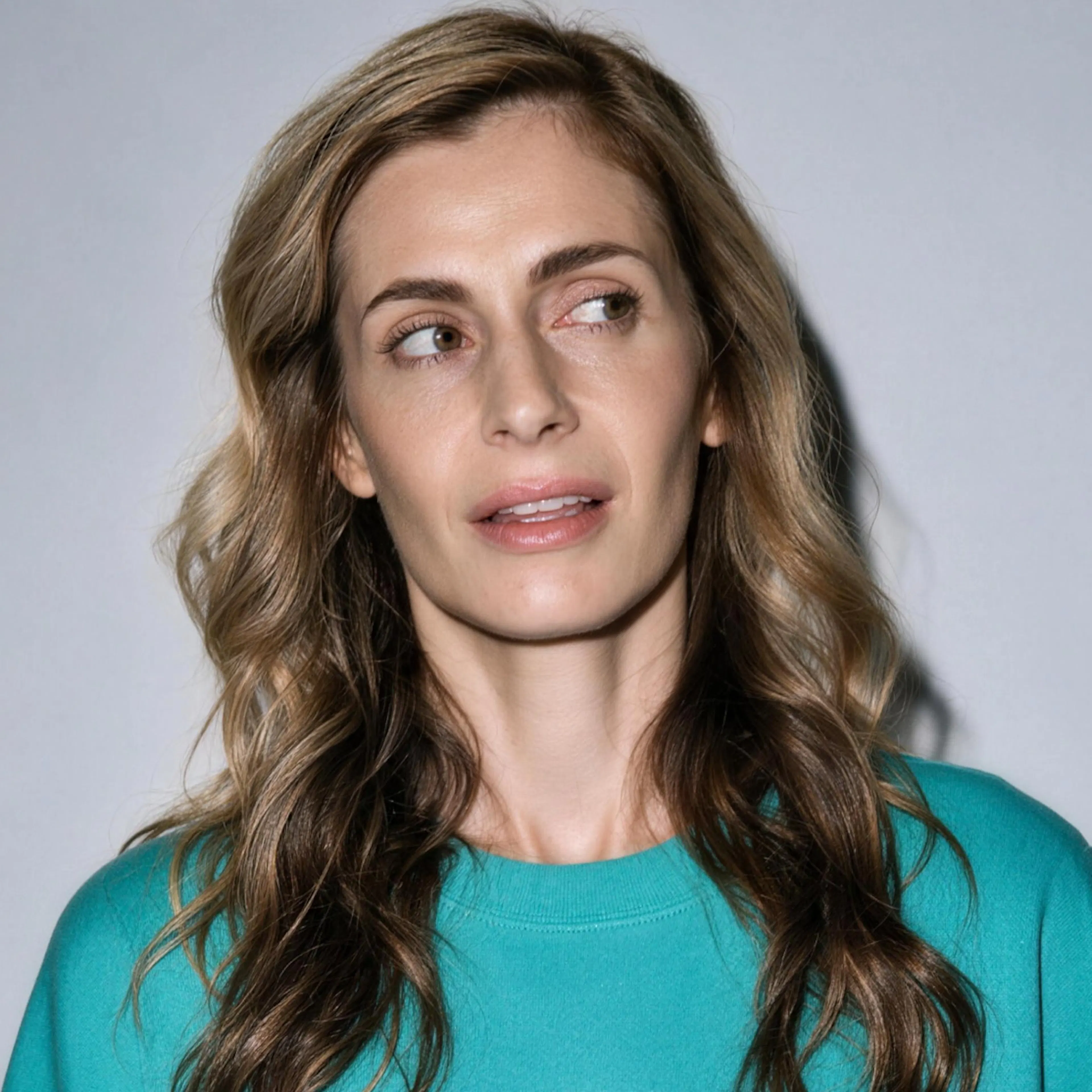 A woman in midlife, feeling irritable, looking to the side. She's wearing a teal sweater.