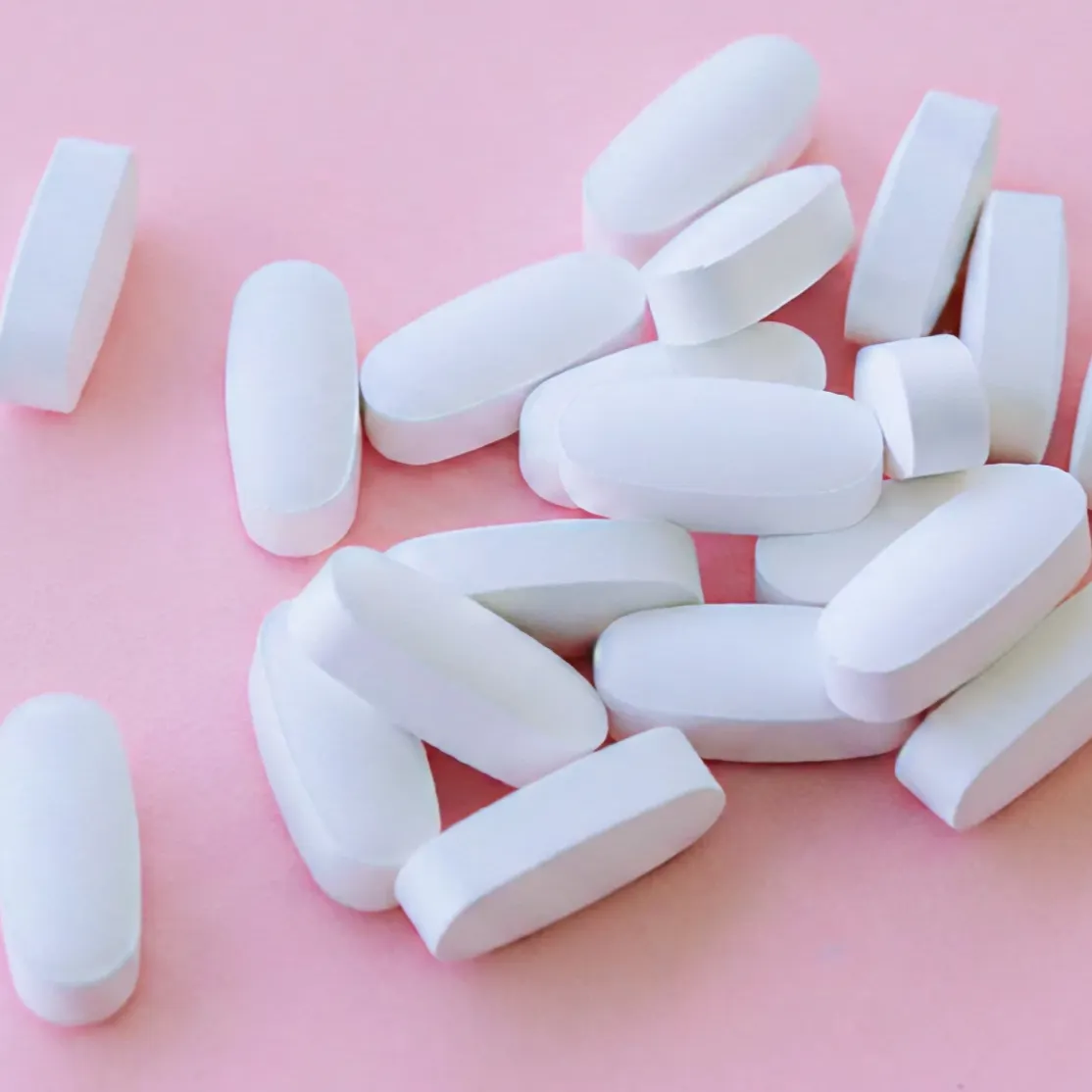 A close-up photo of calcium supplements on a light pink background