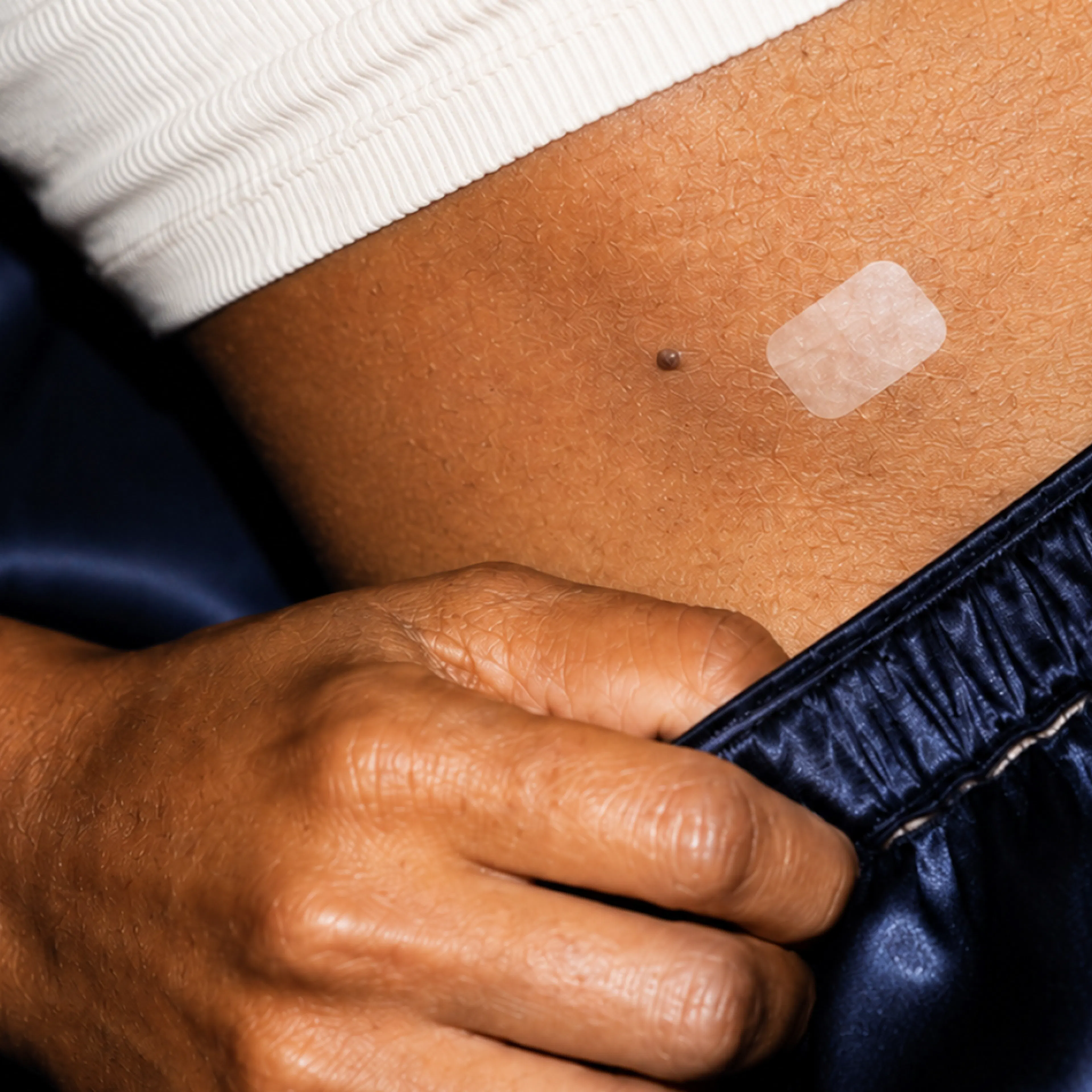 A close-up photo of an estrogen patch on a woman's abdomen.