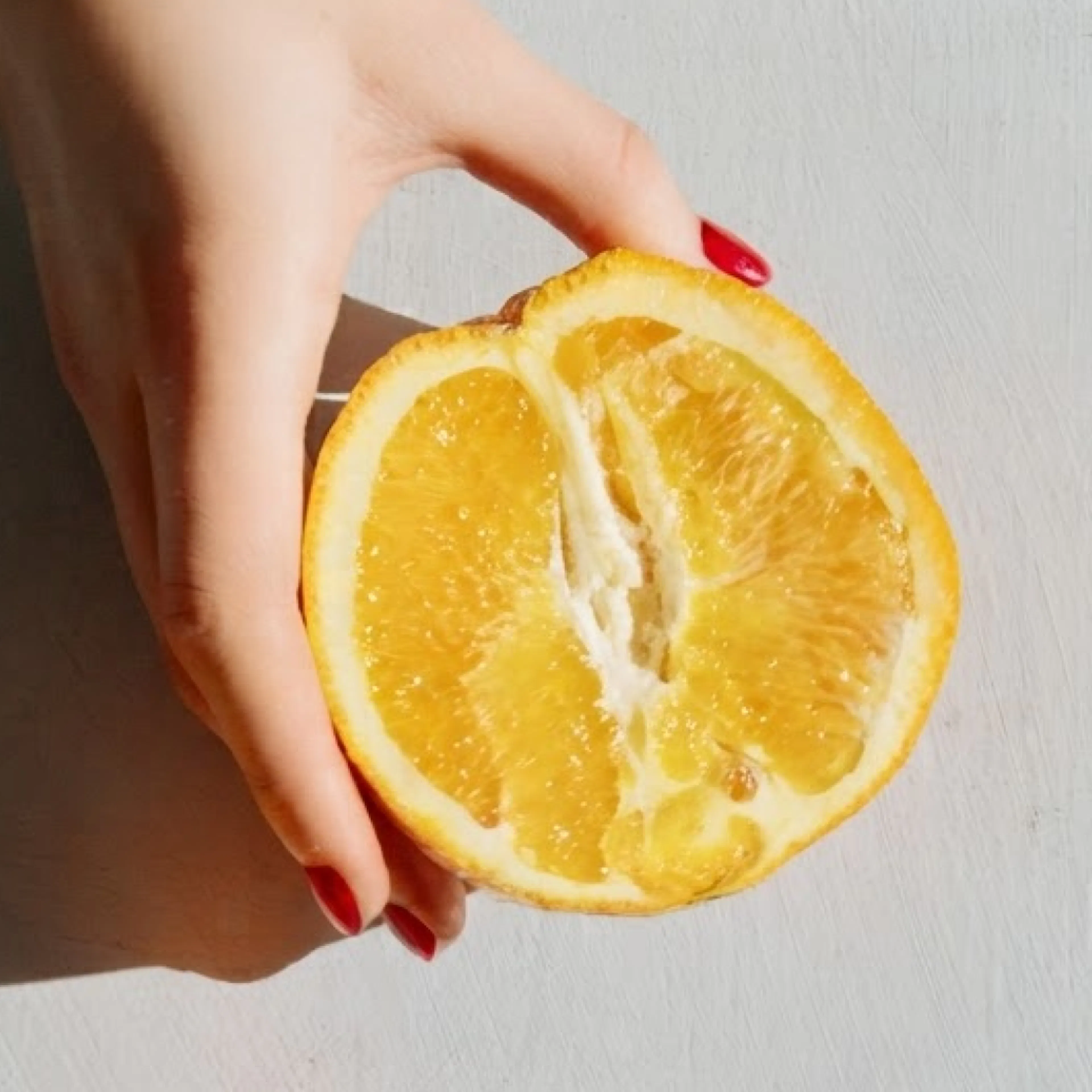 A close-up image of a woman holding a half of an orange.