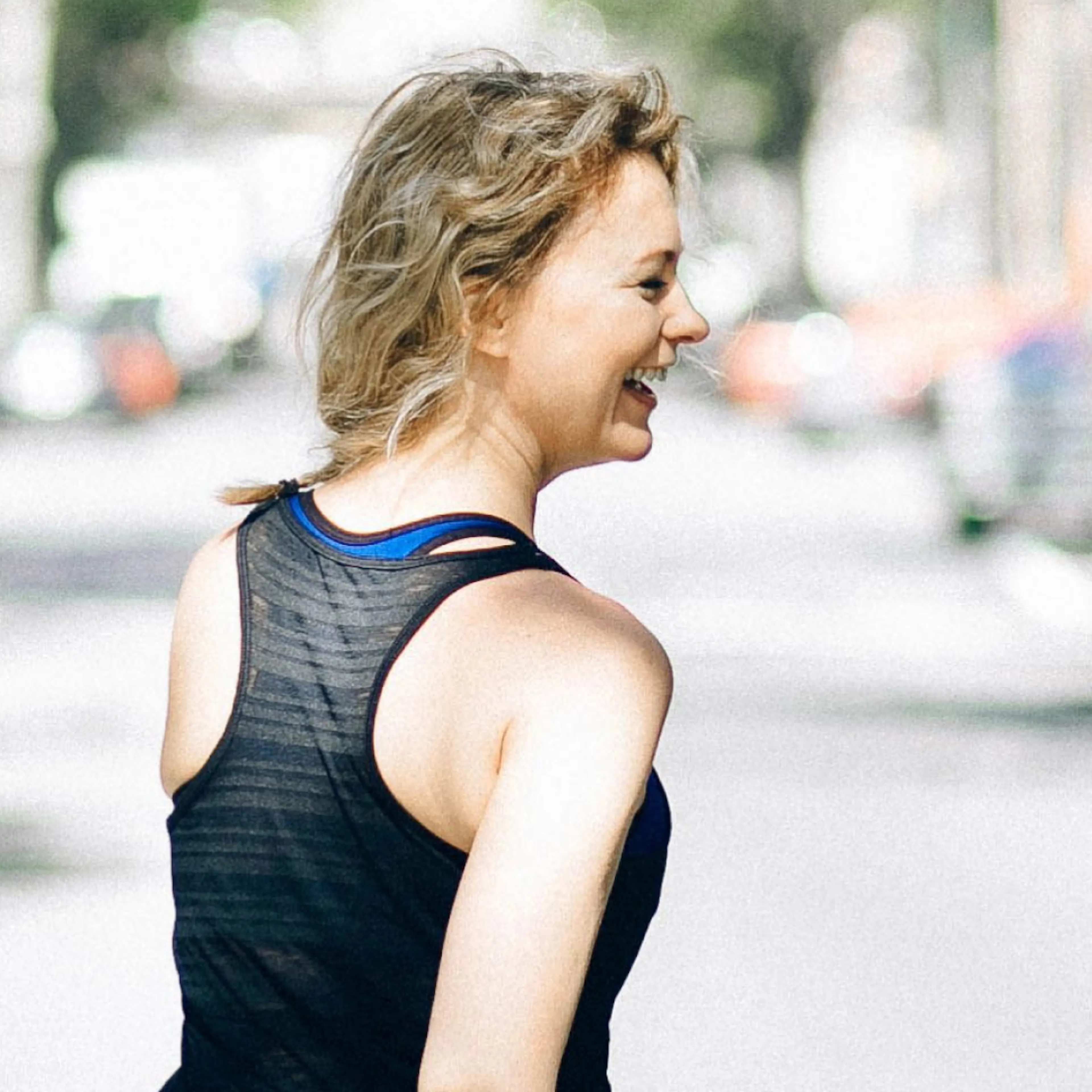 A woman in midlife smiling as she walks outside in a workout tank.