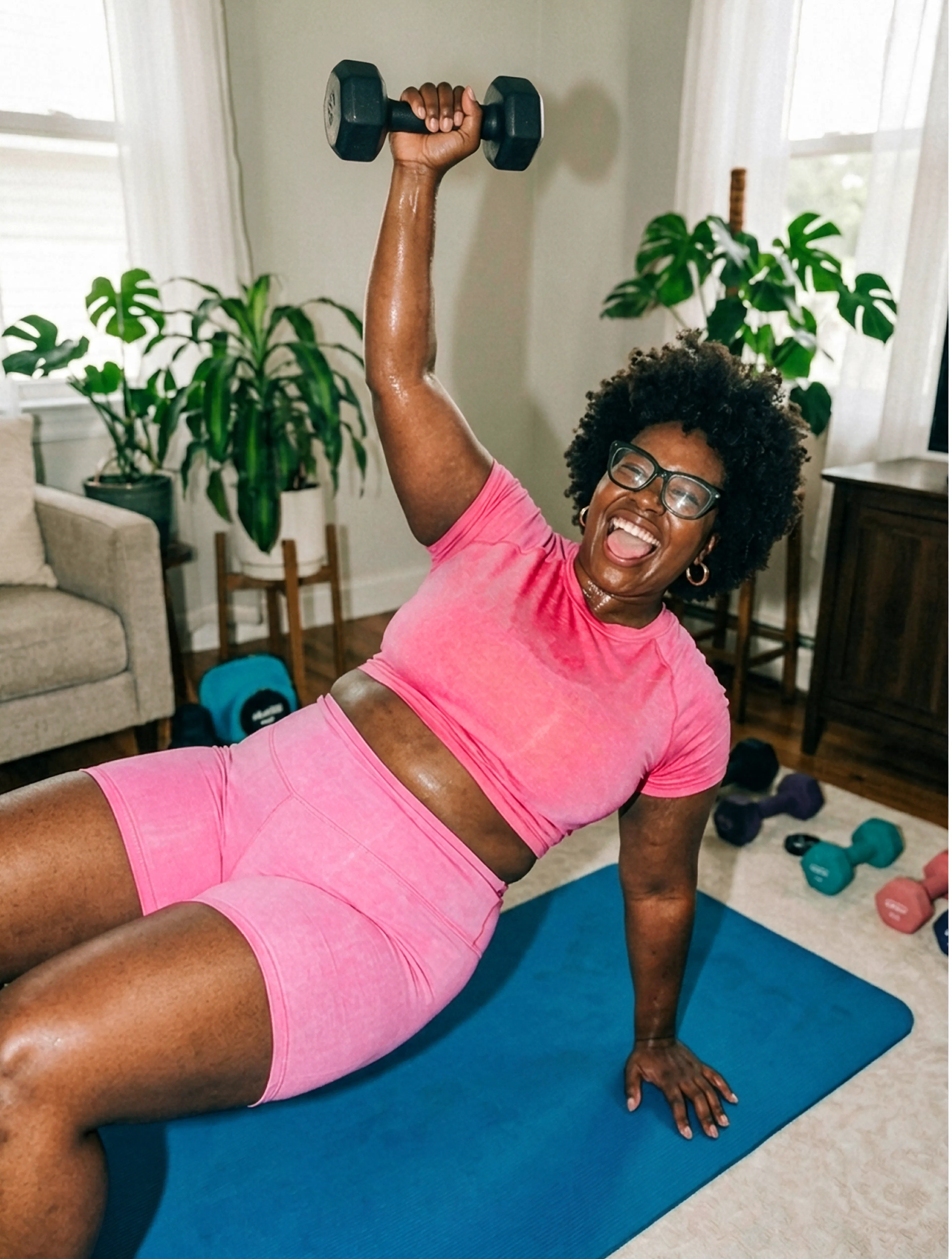 A smiling woman in bright pink activewear pressing a black dumbbell overhead