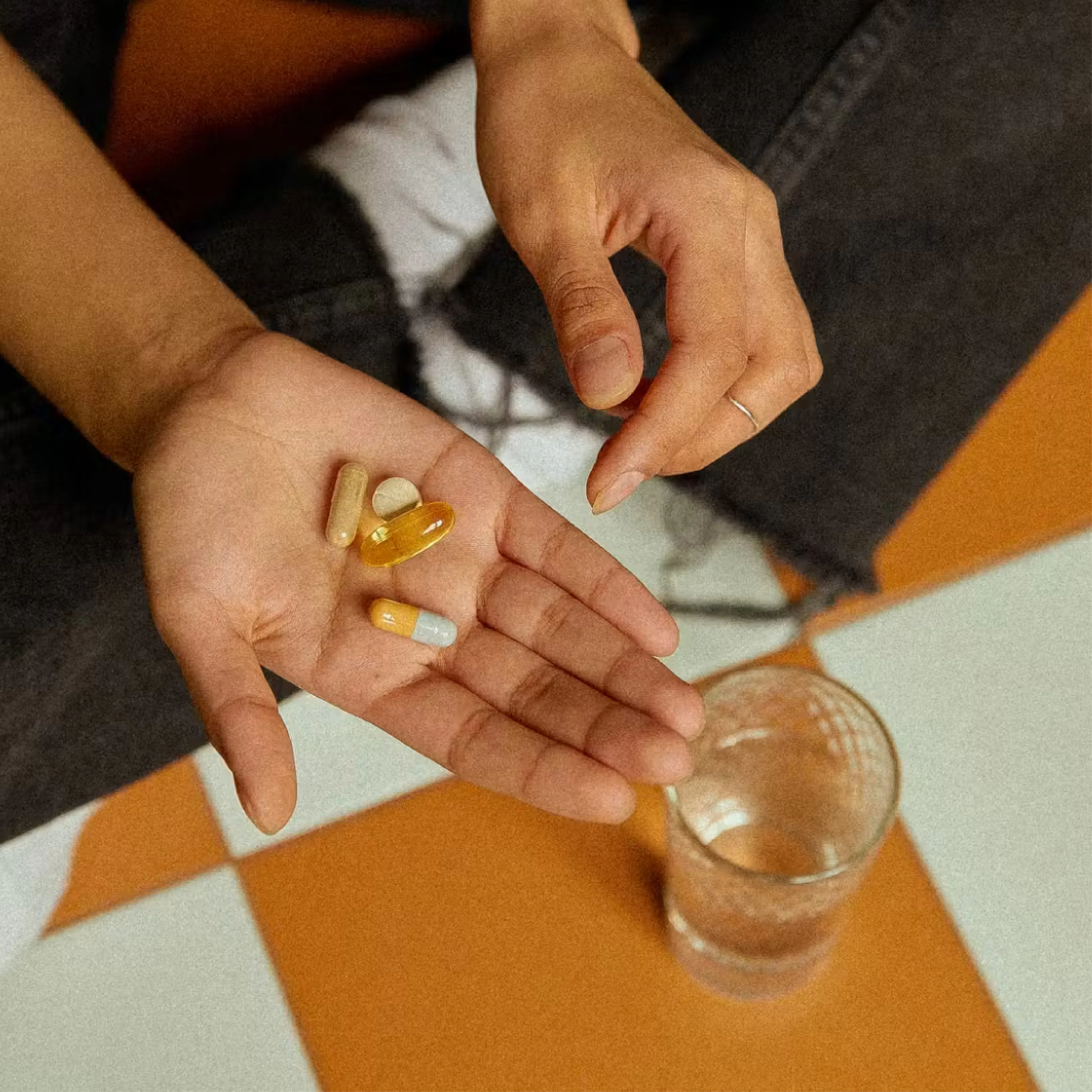 Hand holding colorful pills beside water