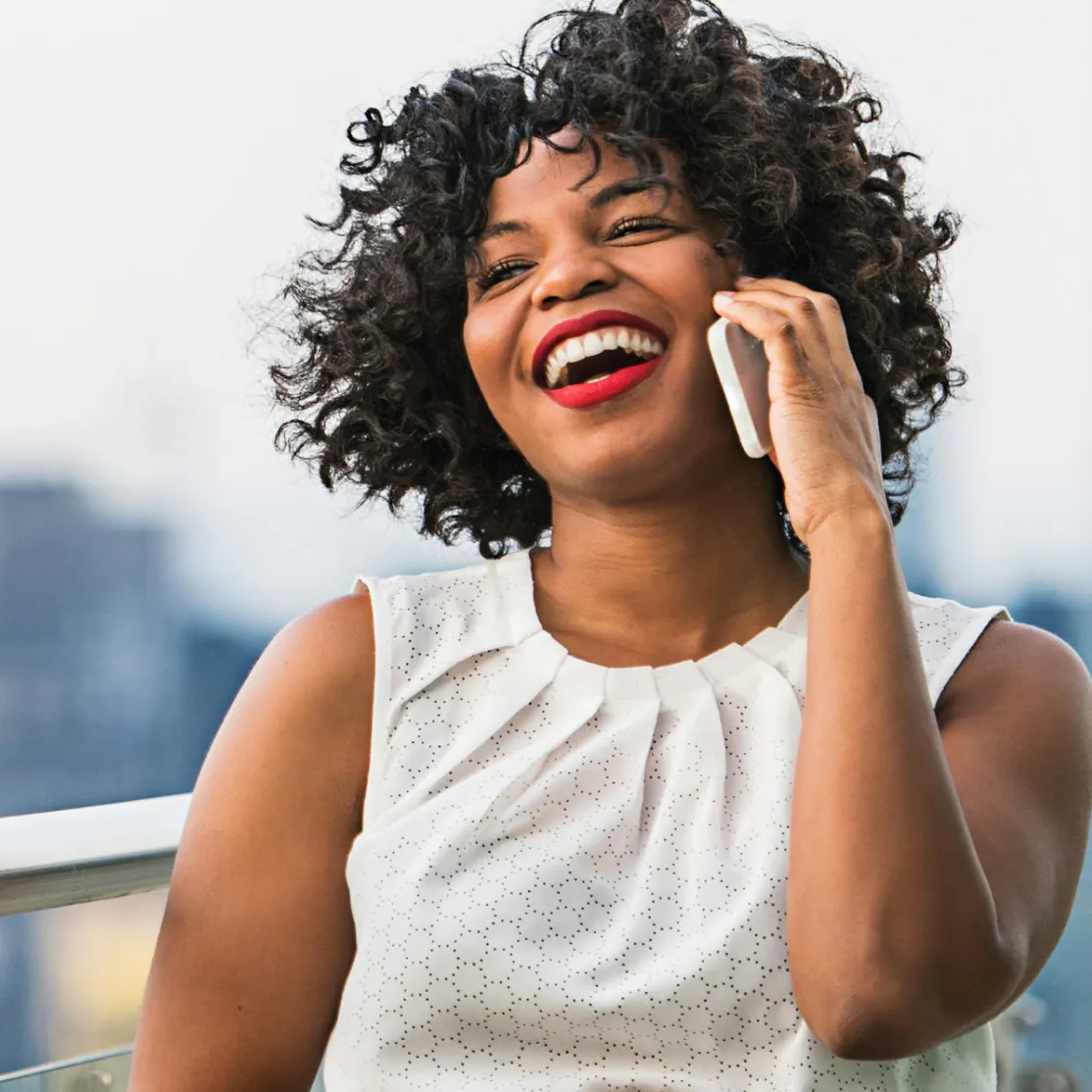 A woman in midlife on the phone, laughing as she sits outside.
