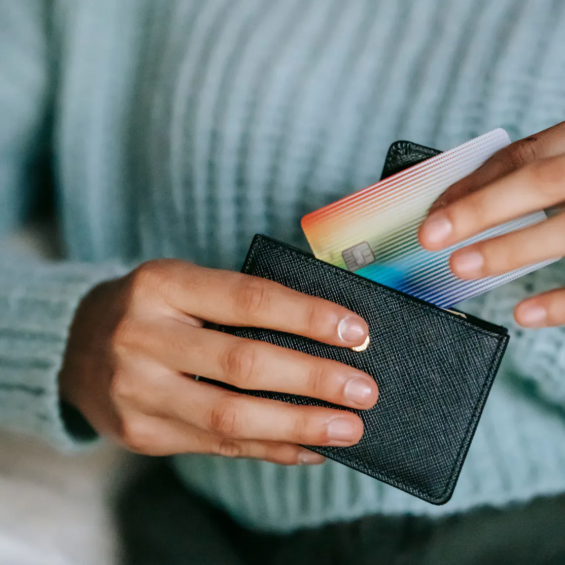 A close-up photo of a woman pulling a credit card out of a black wallet. She's wearing a blue sweater.