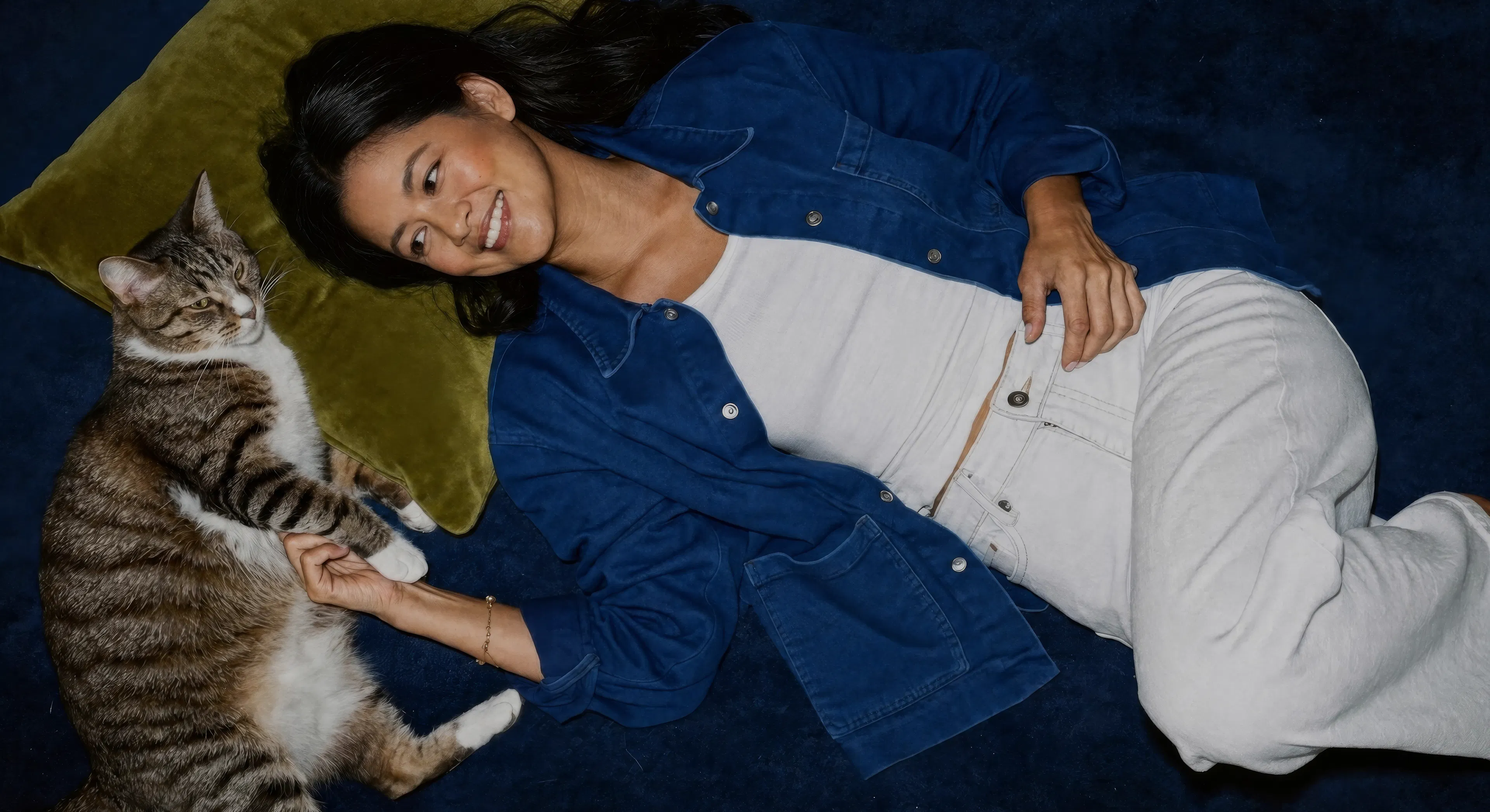 woman laying on the ground on a green pillow with her cat
