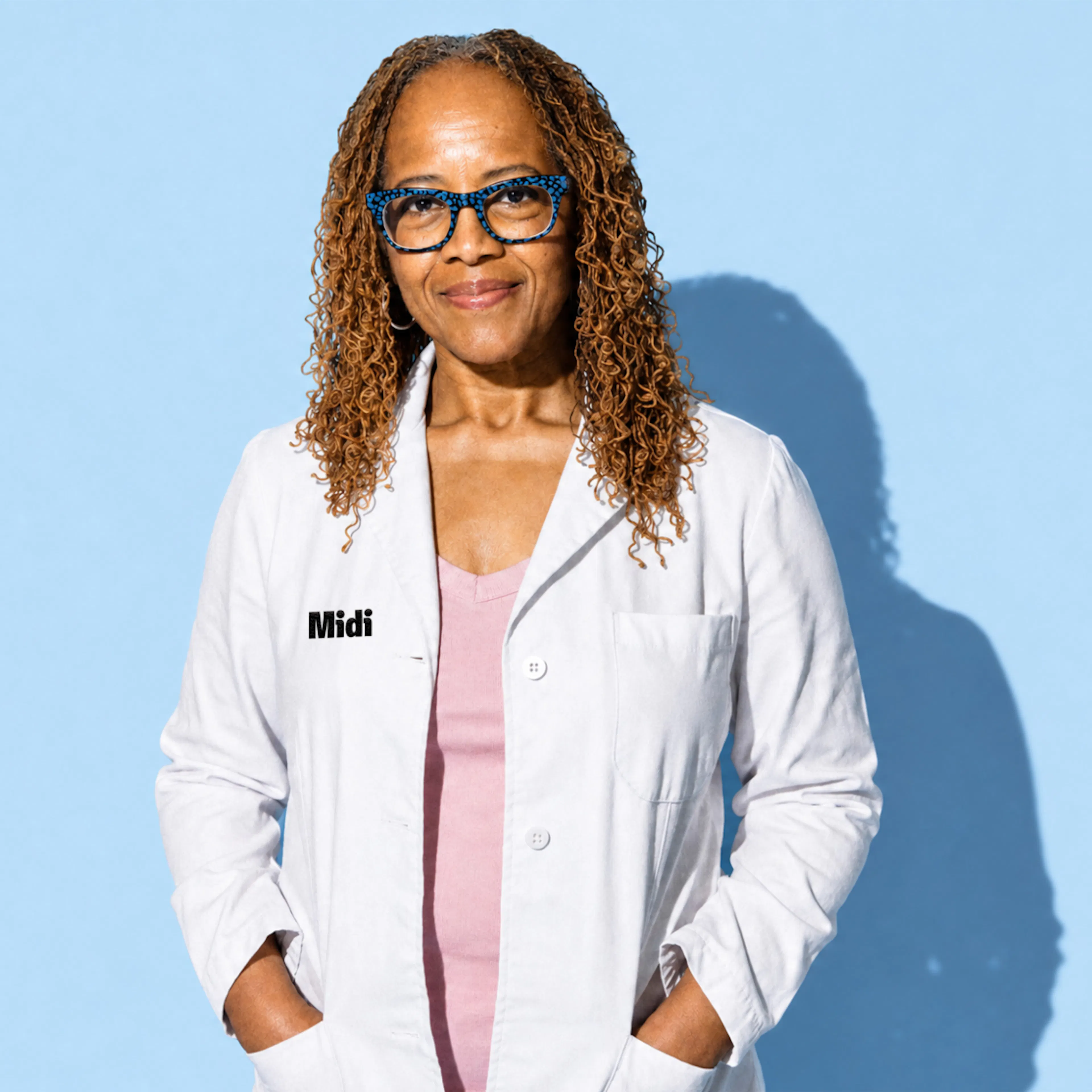 A Midi clinician smiling, wearing a white lab coat and pink scrubs.