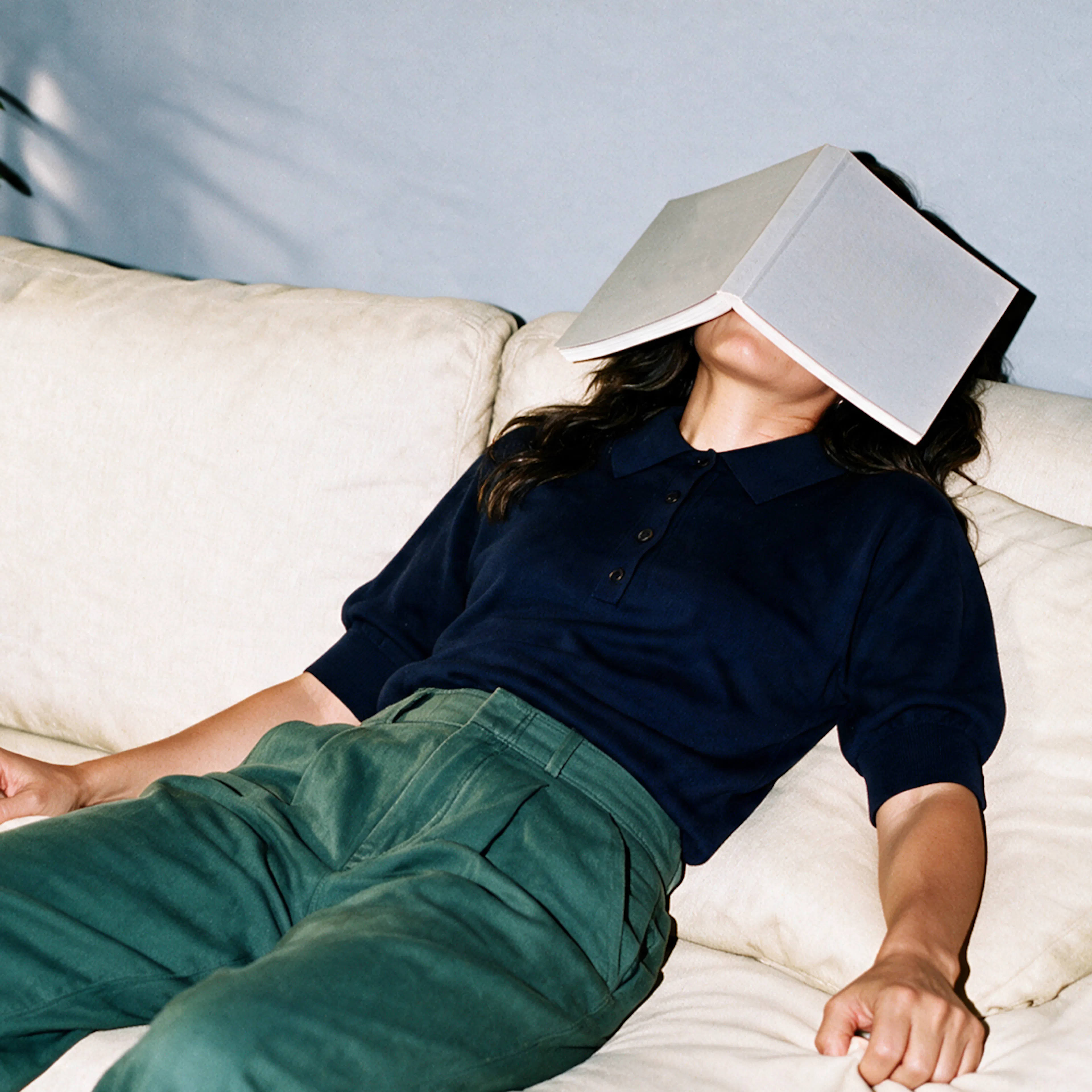 A woman feeling tired, perhaps after taking her progesterone. She is lying down on a couch with a book on her head.