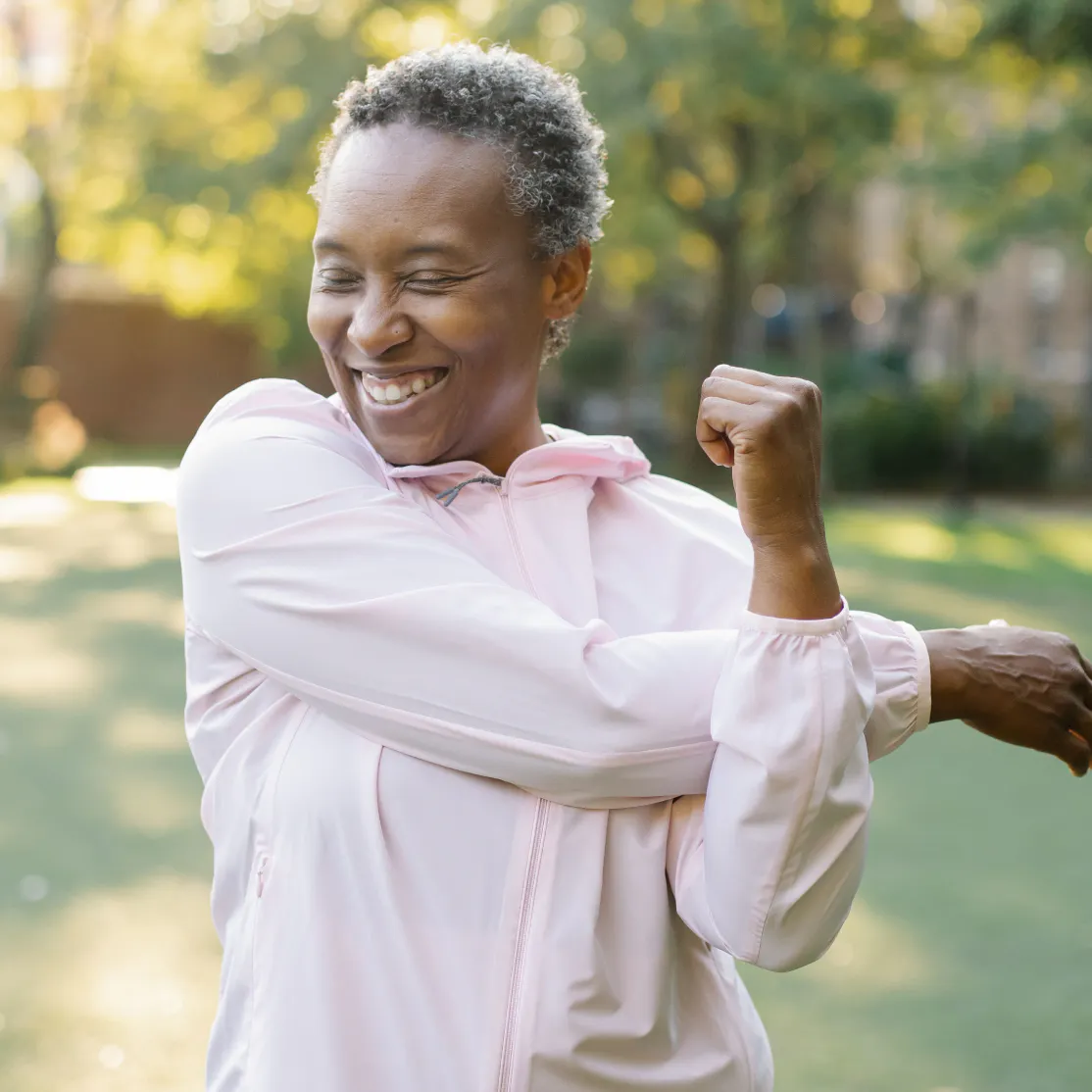 A woman in midlife stretching her arms outside.