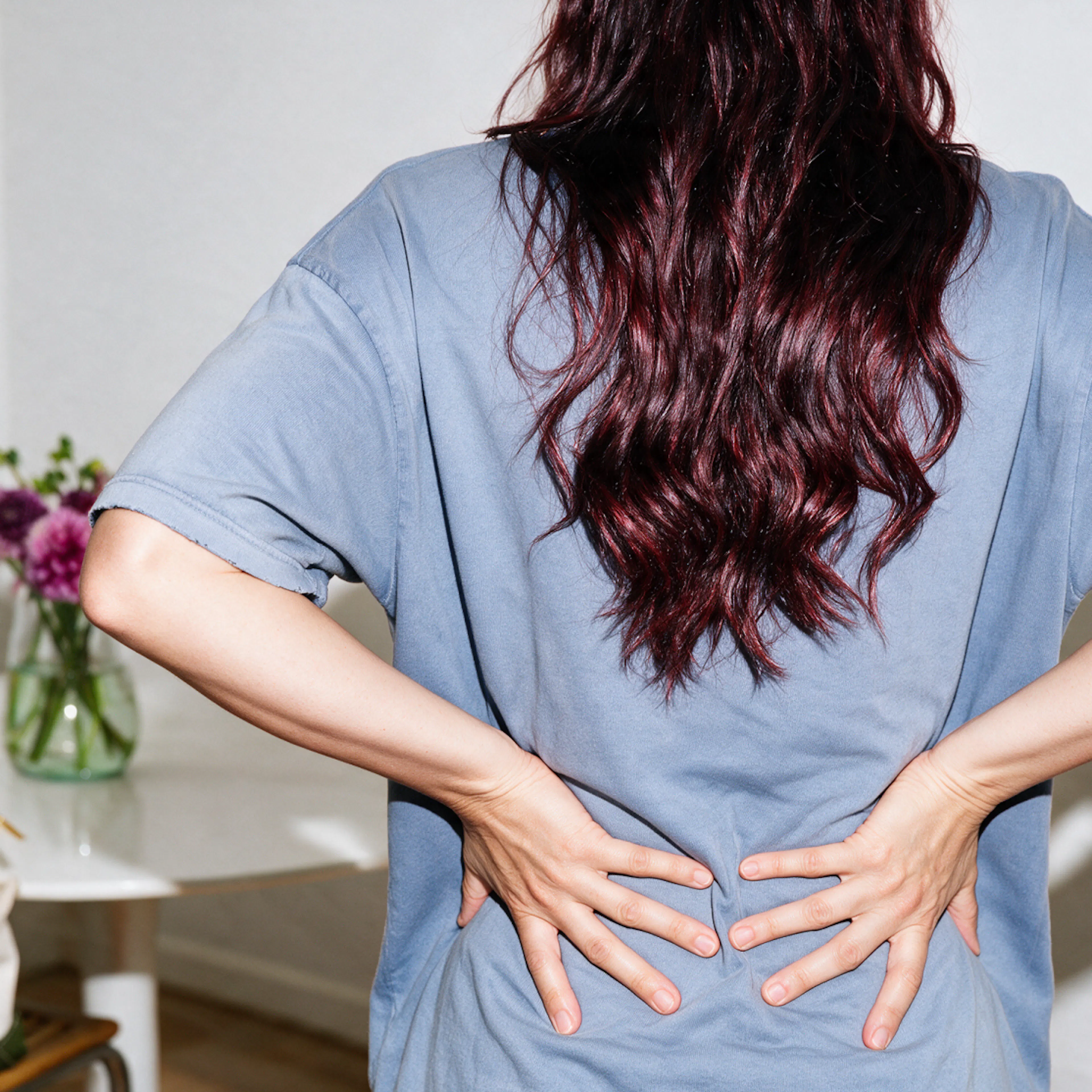 A woman in midlife experiencing back pain. Her hands are on her lower back as she faces forward.