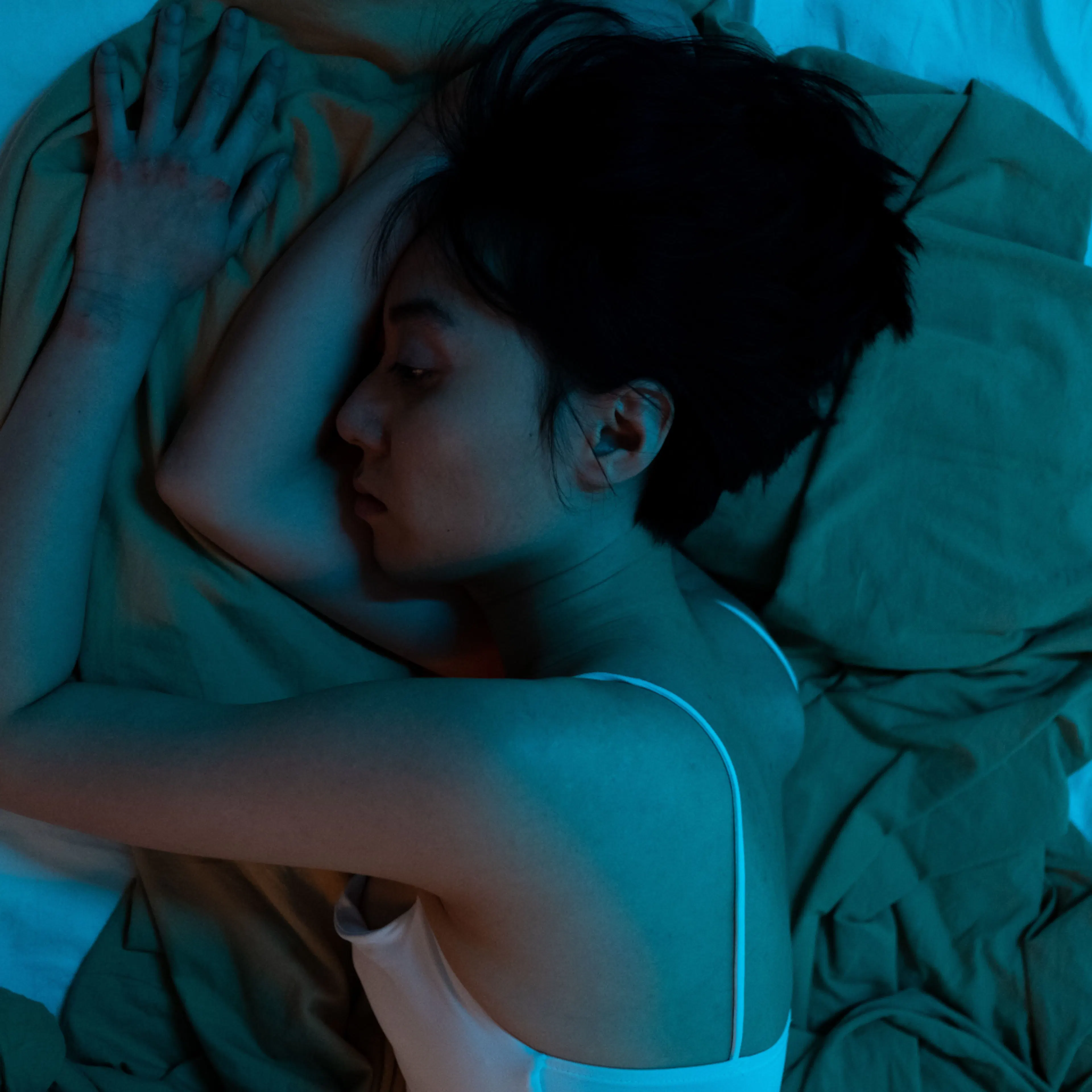 A woman in midlife, sleeping at night in a tank top.