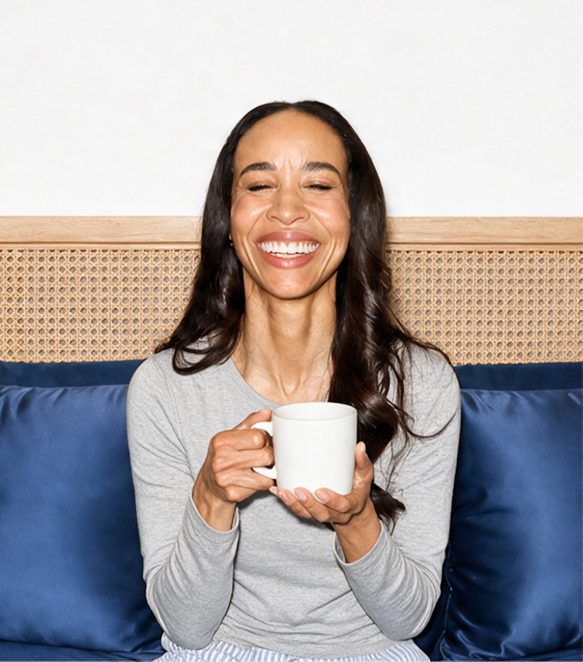An image of a smiling woman in midlife, closing her eyes and holding a cup of coffee while relaxing.